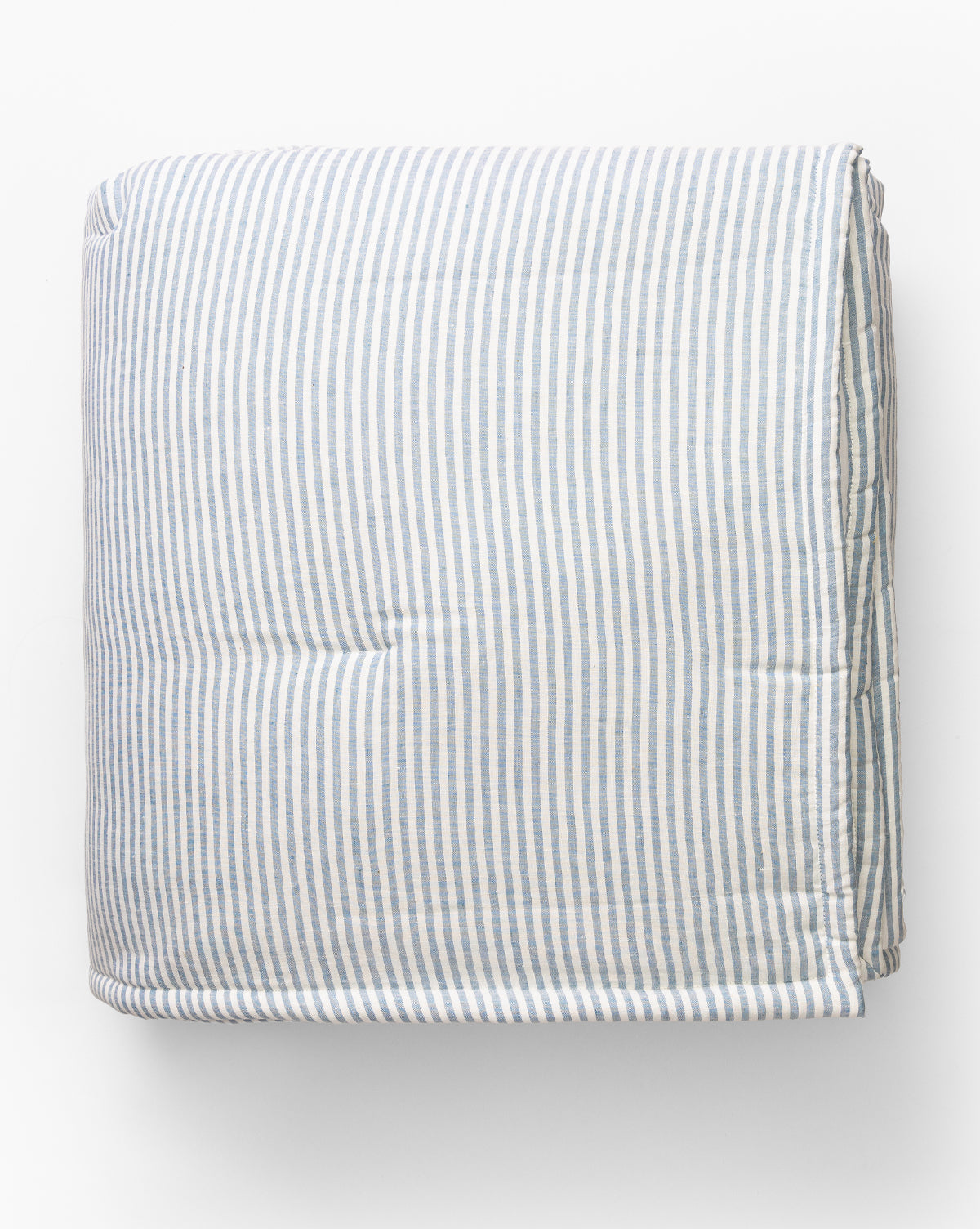 The Rosemary Quilt, made from yarn-dyed linen and cotton, features light blue and white vertical stripes and is neatly folded against a plain white background.