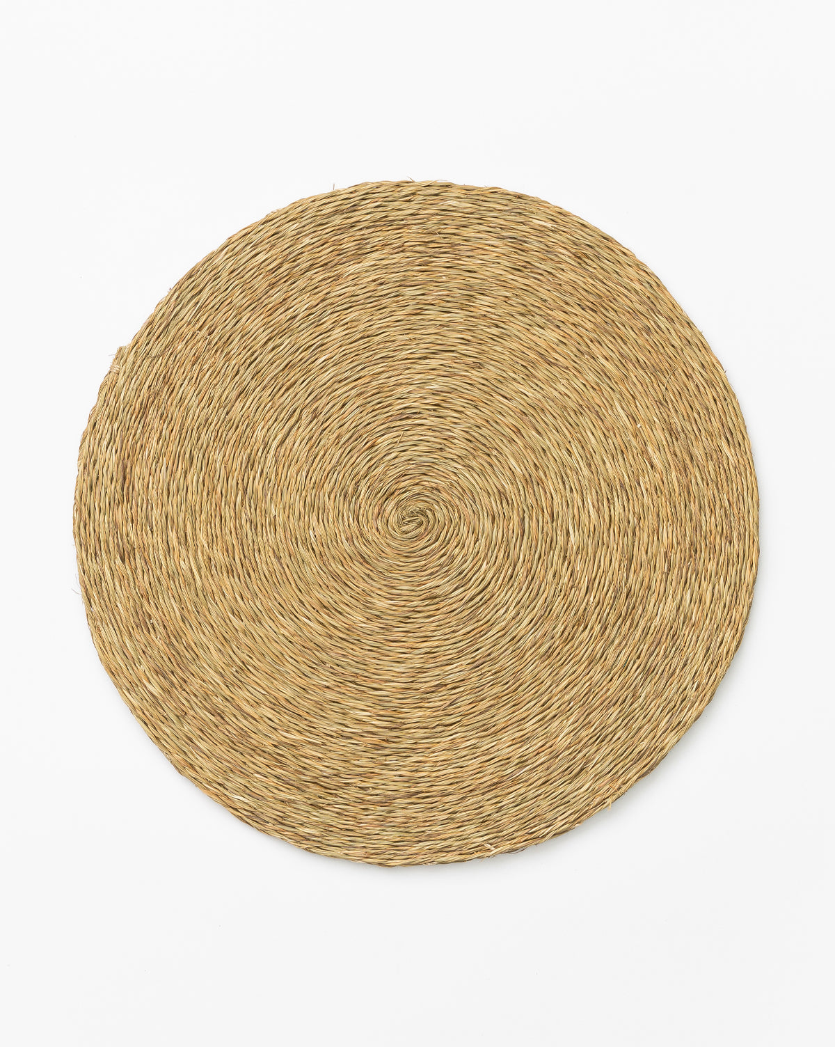 The Round Woven Placemat, handcrafted from natural Lutindzi grass, is shown on a white background. Waterproof, it brings organic elegance and durability to any table setting, by McGee & Co.