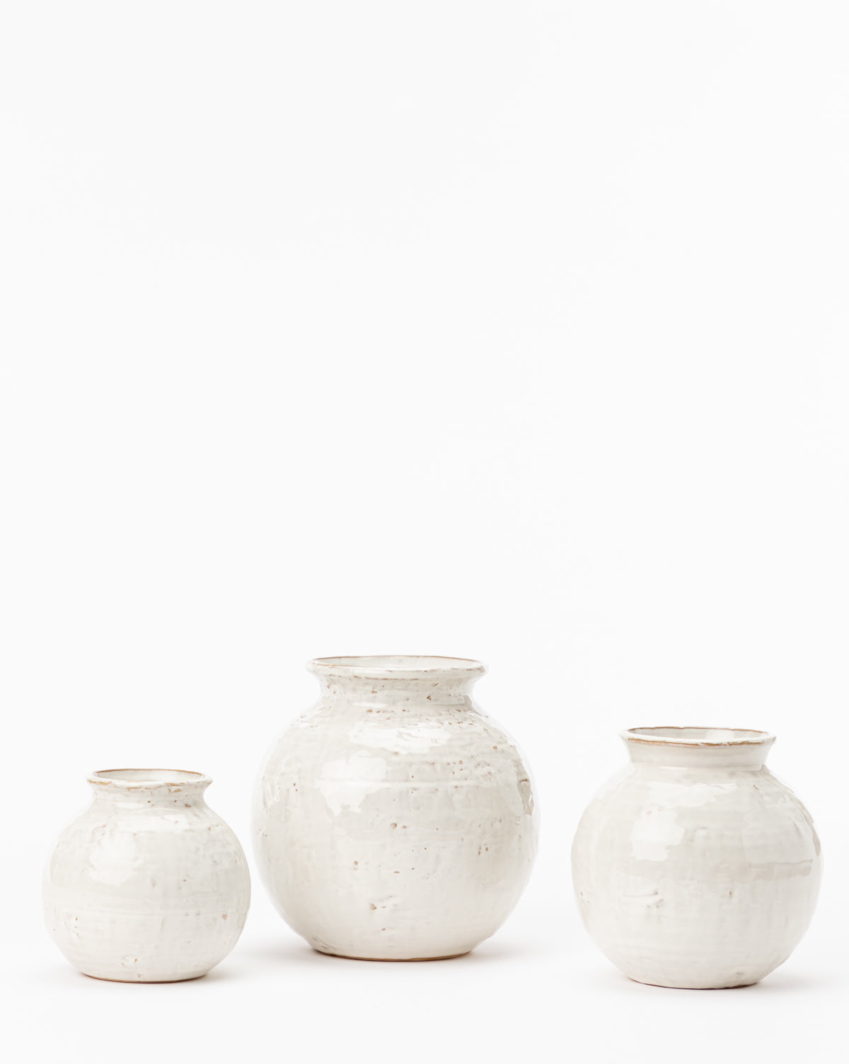 Three white Rounded Ceramic Vases, each with a slightly textured, distressed glaze and varying heights, are stylishly arranged side by side on a white background—perfect for elevating your home decor.