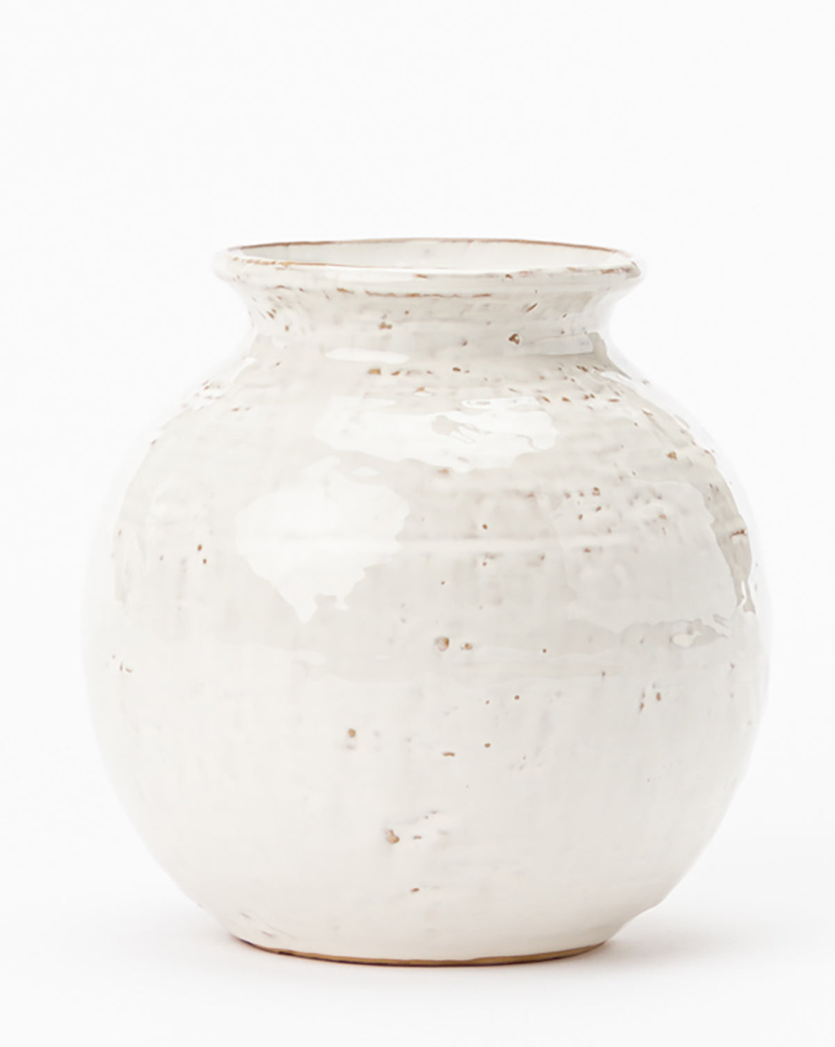 The Rounded Ceramic Vase is a white, round ceramic decor piece featuring a wide body, narrow neck, flared rim, and a glossy distressed glaze with subtle brown speckles.