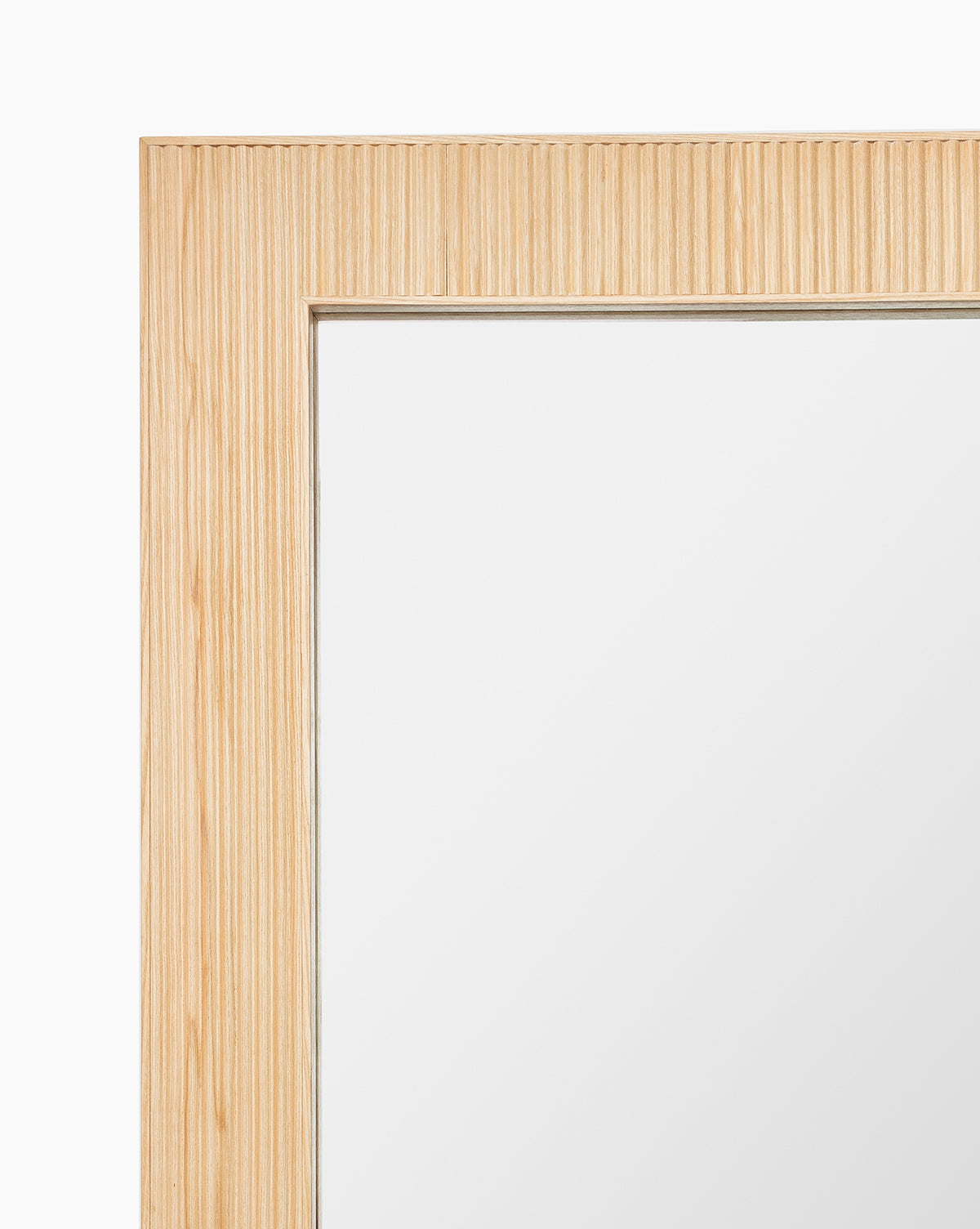 Close-up of the Rowan Wall Mirror’s top left corner, highlighting its ribbed ash wood frame with vertical grooves, set against a white background, by McGee & Co.
