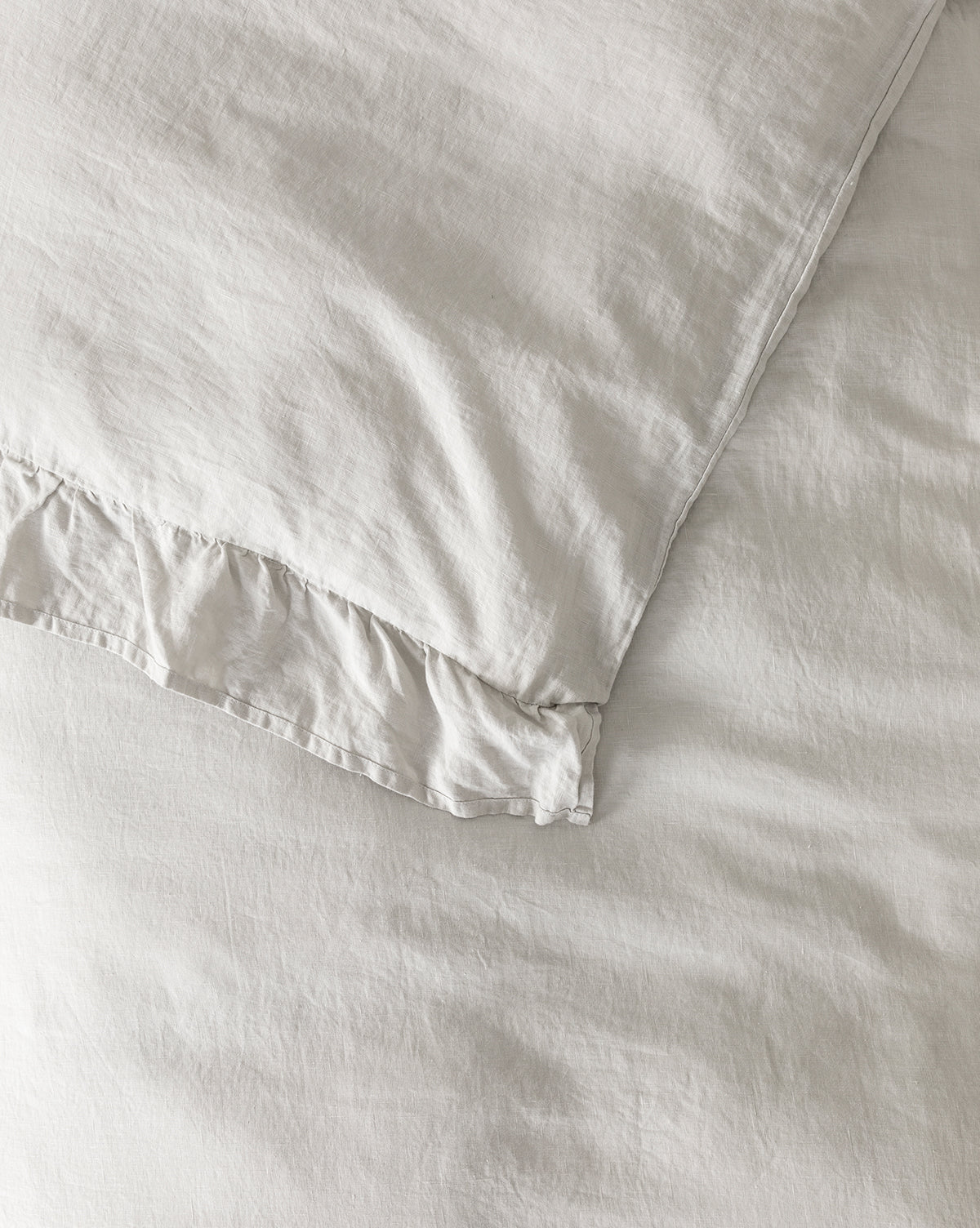 Close-up of the Ruffle Linen Duvet Cover, crafted from 100% linen with subtle ruffled edges, shown resting on a matching smooth bed sheet. The slightly textured fabric adds a soft and inviting touch to your bedding.