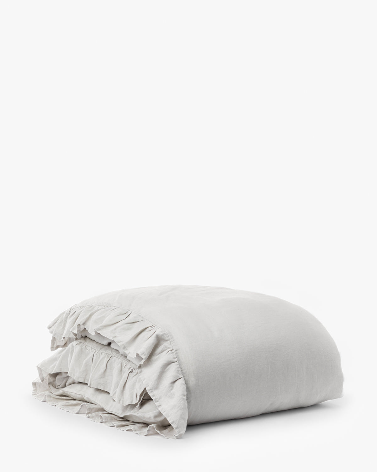 The Ruffle Linen Duvet Cover, made from 100% linen in light gray with ruffled edges, is neatly folded and displayed on a white background.