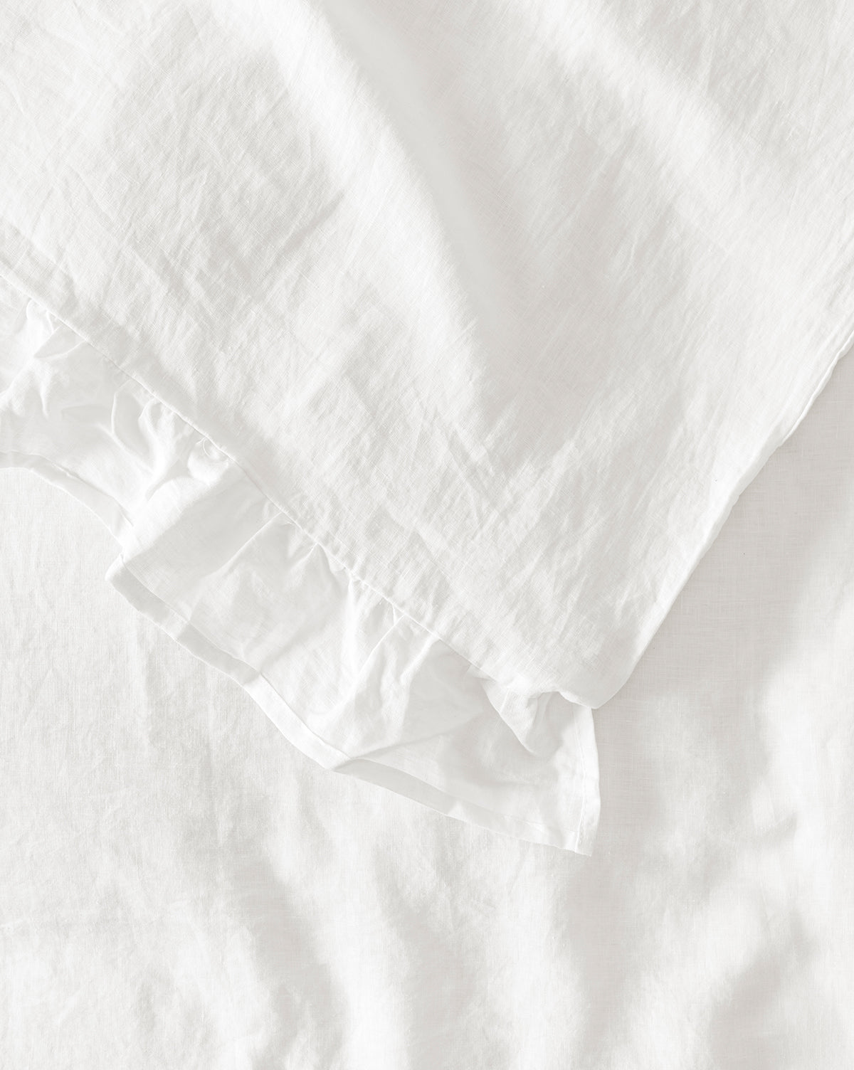 A close-up of the Ruffle White Linen Duvet Cover reveals its 100% linen fabric, featuring a ruffled edge and naturally wrinkled texture for a soft, inviting look.