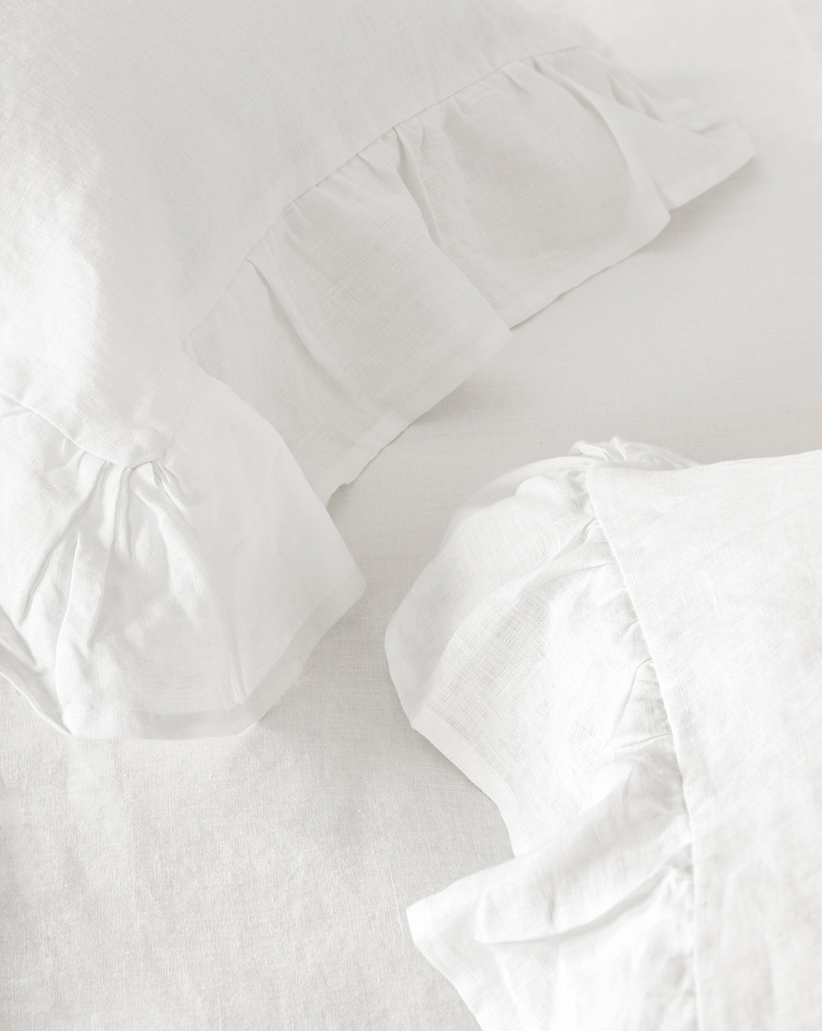Ruffle White Linen Shams (Set of 2) rest on a matching white linen bed sheet, offering 100% linen pillow shams with soft ruffled edges for an elegant bedding arrangement.