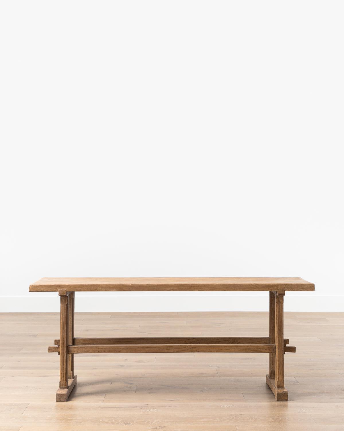 The Rufus Console Table, made from reclaimed elm with a rectangular top and trestle base, is shown on a light wood floor against a plain white wall, by McGee & Co.