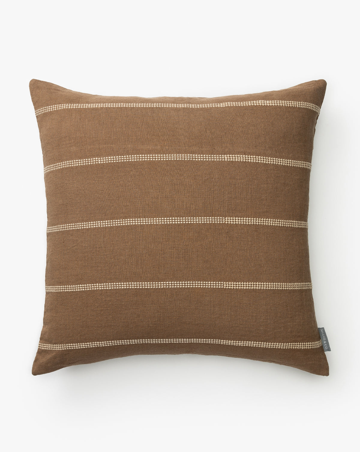 The Ryder Pillow Cover is a square brown case with horizontal beige stitched stripes and a small fabric tag on one side, shown against a plain white background by McGee & Co.