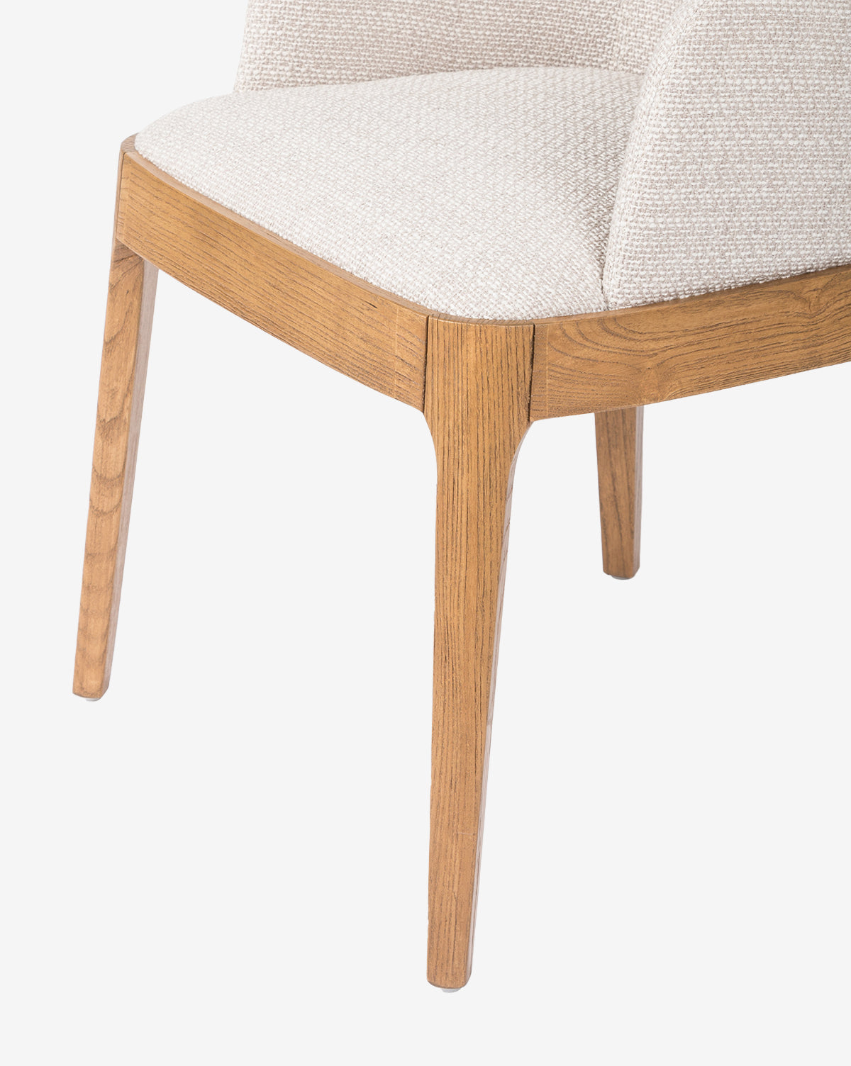 Close-up of the Ryne Dining Chair, a modern design with light beige upholstered seat and backrest, set on solid oak legs and frame in a natural finish, shown against a white background by McGee & Co.