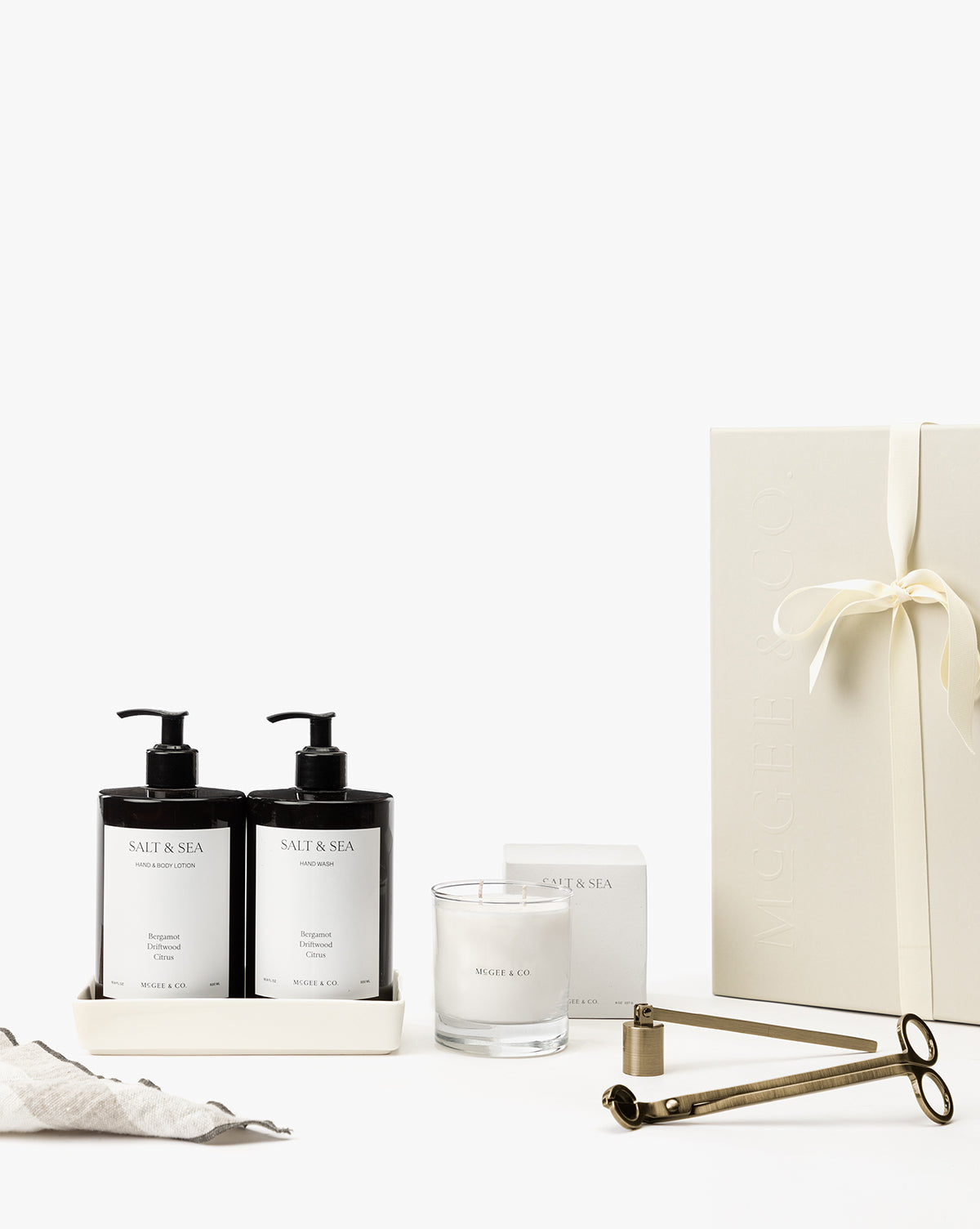 The Salt & Sea Gift Set features two pump bottles, a candle, a wick trimmer, and a ribbon-tied white box with minimalist white labels—ideal for bringing the signature scent of calm to your home spa, by McGee & Co.