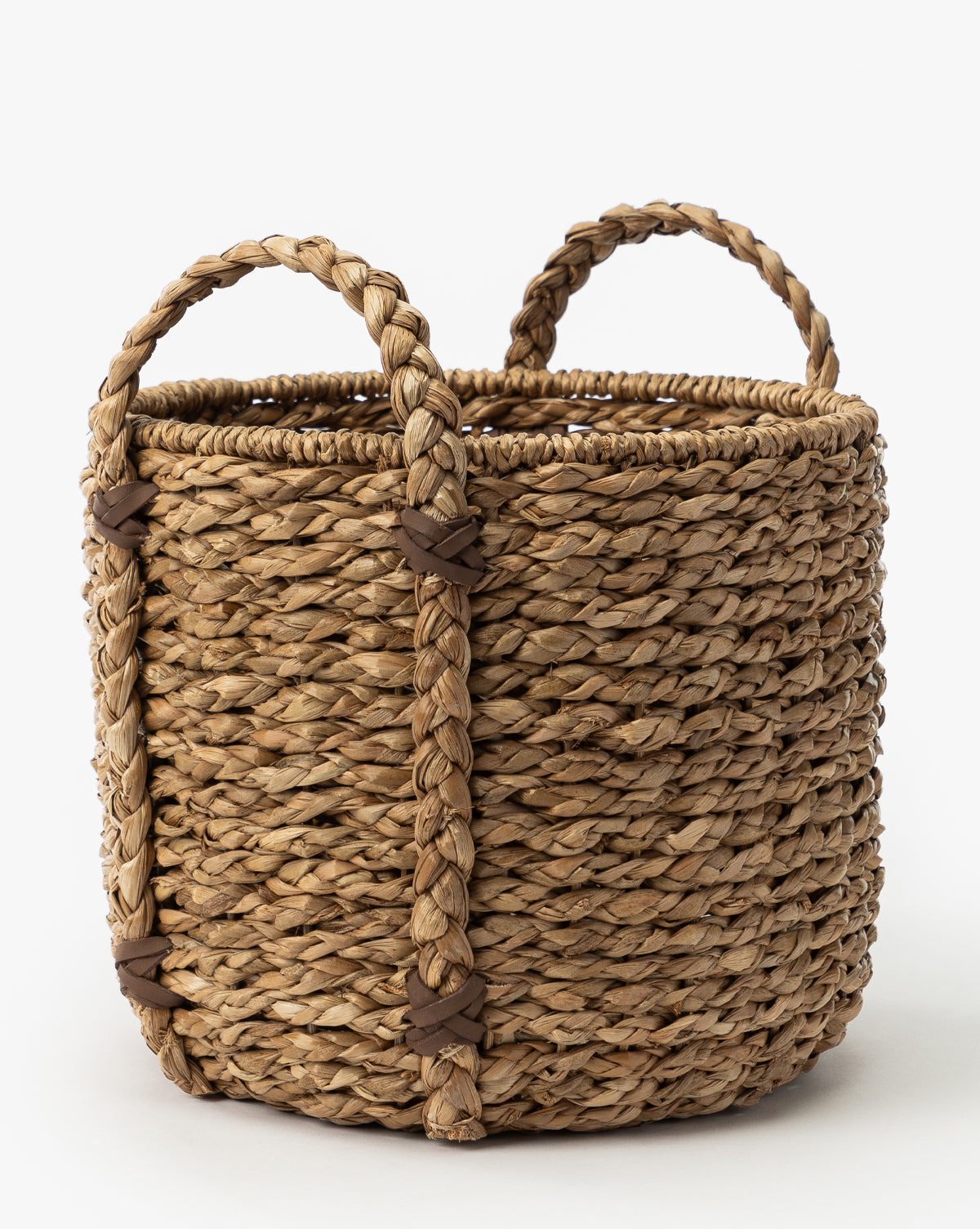 The Salter Woven Basket is a round seagrass basket made from natural fibers, featuring two braided handles with brown leather-like bands, shown on a white background by McGee & Co.