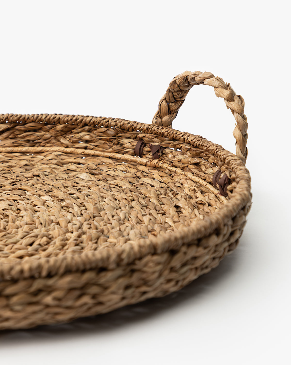 A close-up of the Salter Woven Tray, a round straw storage tray with a braided handle, displayed on a white background, by McGee & Co.