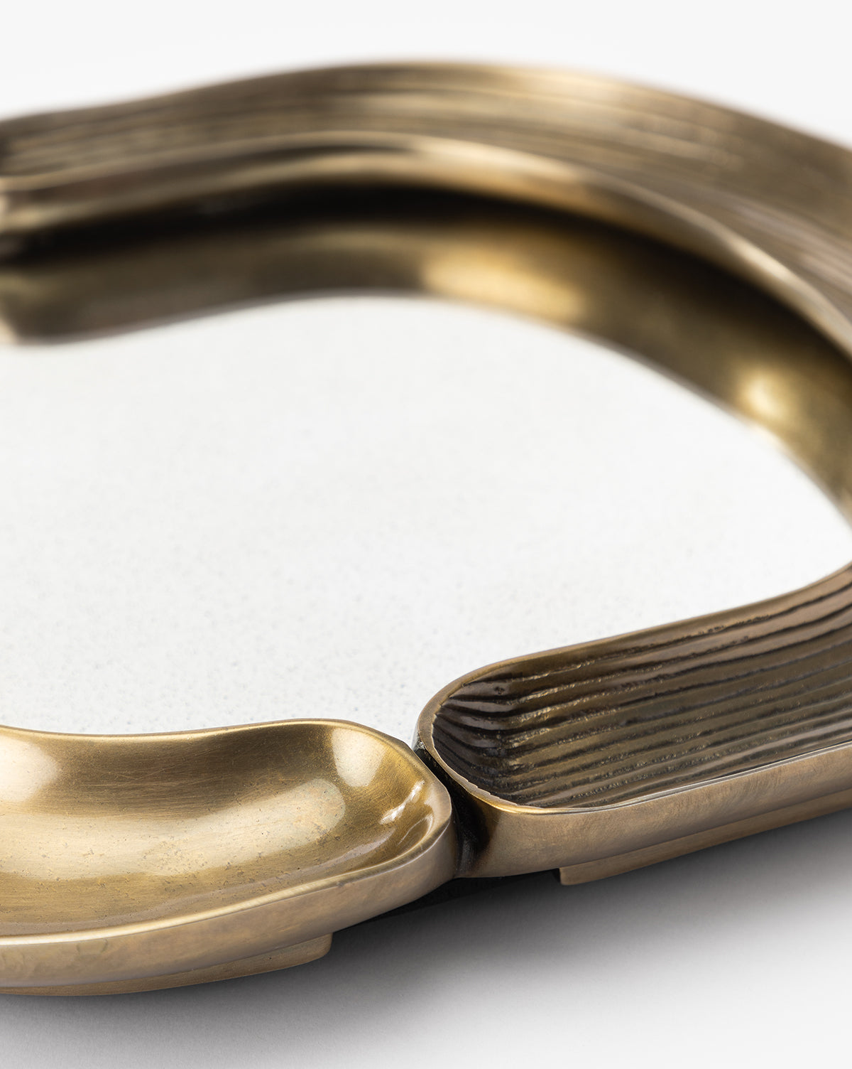 A close-up of the Salvatore Wall Mirror, featuring curved, textured brass sections and a smooth white center. Its artistic, modern design showcases an antique gold finish with a mix of matte and shiny surfaces by McGee & Co.