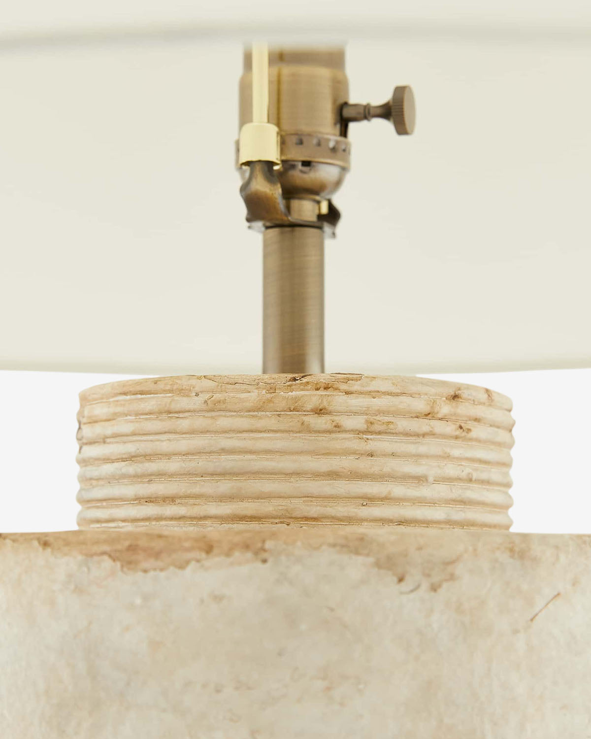 Close-up of the Samala Lamp, featuring a textured stone-like base with horizontal grooves for a vintage look, topped with a brass socket and partially shaded by a white lampshade by McGee & Co.