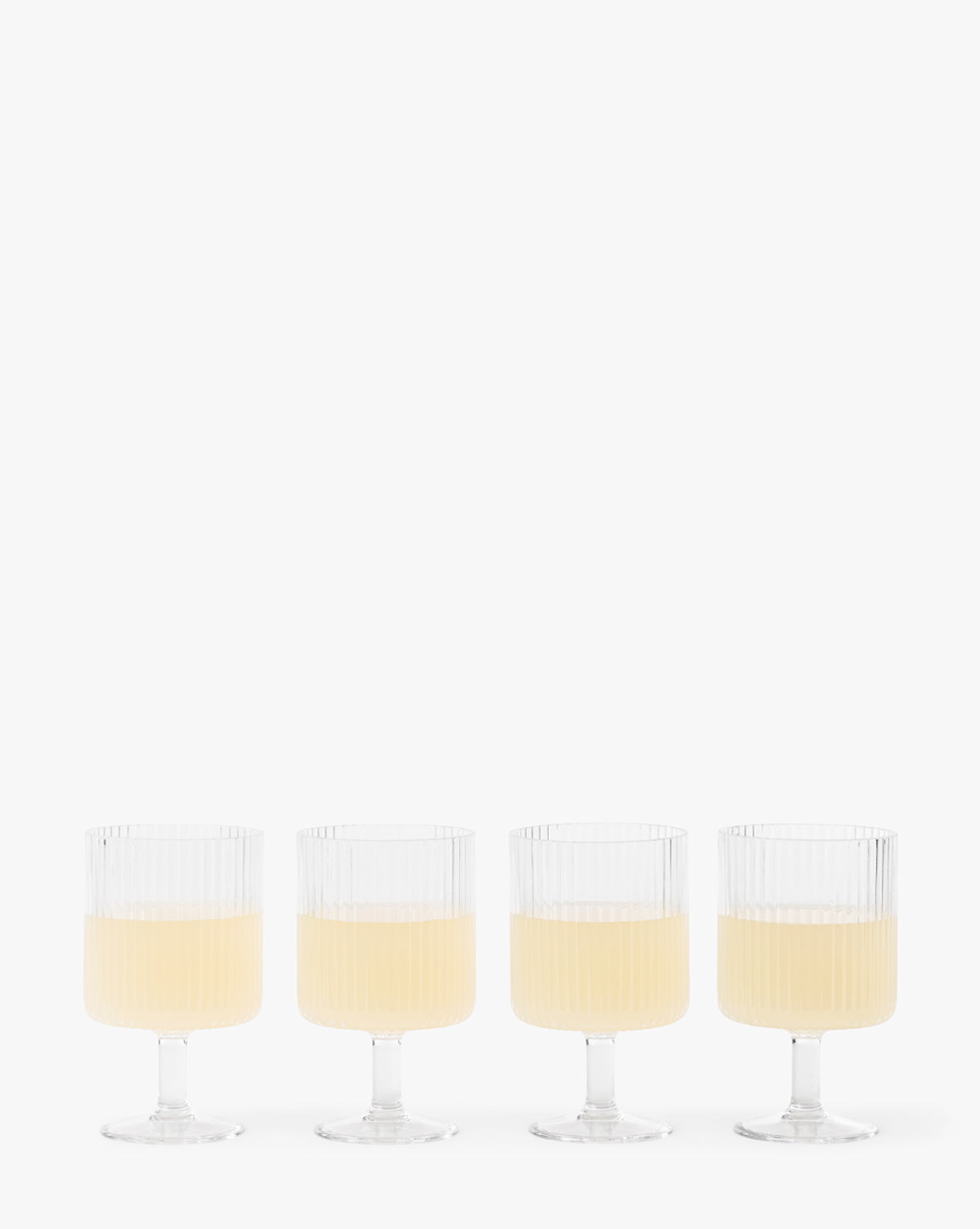The Sanibel Acrylic Goblets (Set of 4) feature clear, ribbed designs and short stems, each filled halfway with a light yellow drink—ideal for stylish outdoor table settings against a simple white background.