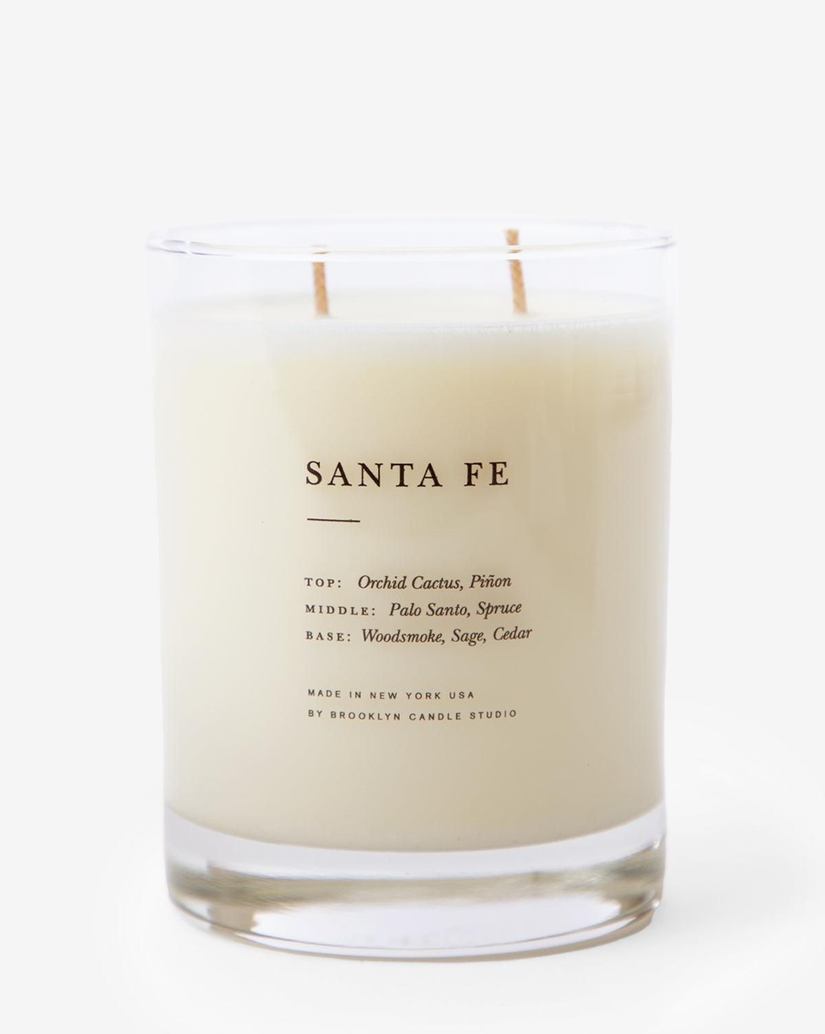 The Santa Fe Candle is a white soy wax candle in a clear glass jar, blending orchid cactus, piñon, palo santo, spruce, woodsmoke, sage, and cedar notes. The label reads Santa Fe Candle with Brooklyn Candle Studio branding.