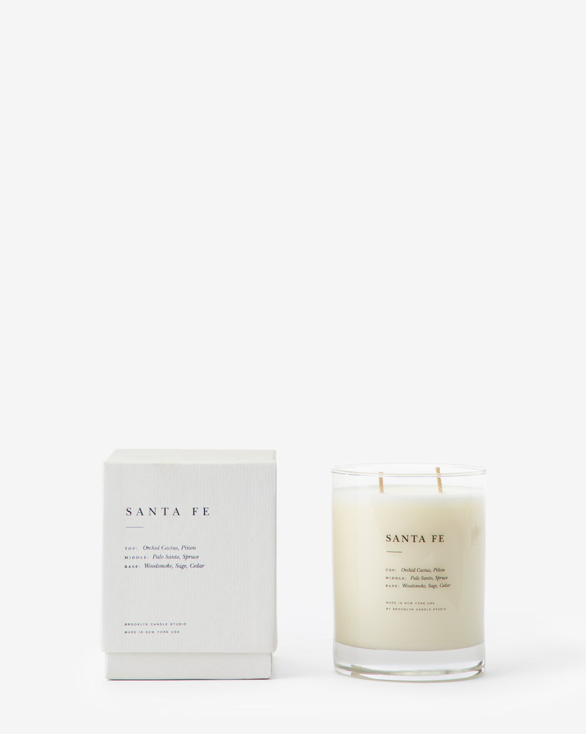 The Santa Fe Candle, crafted from soy wax, comes in a clear glass jar with a matching minimalist box. Both display simple text listing the scent notes, which include palo santo.