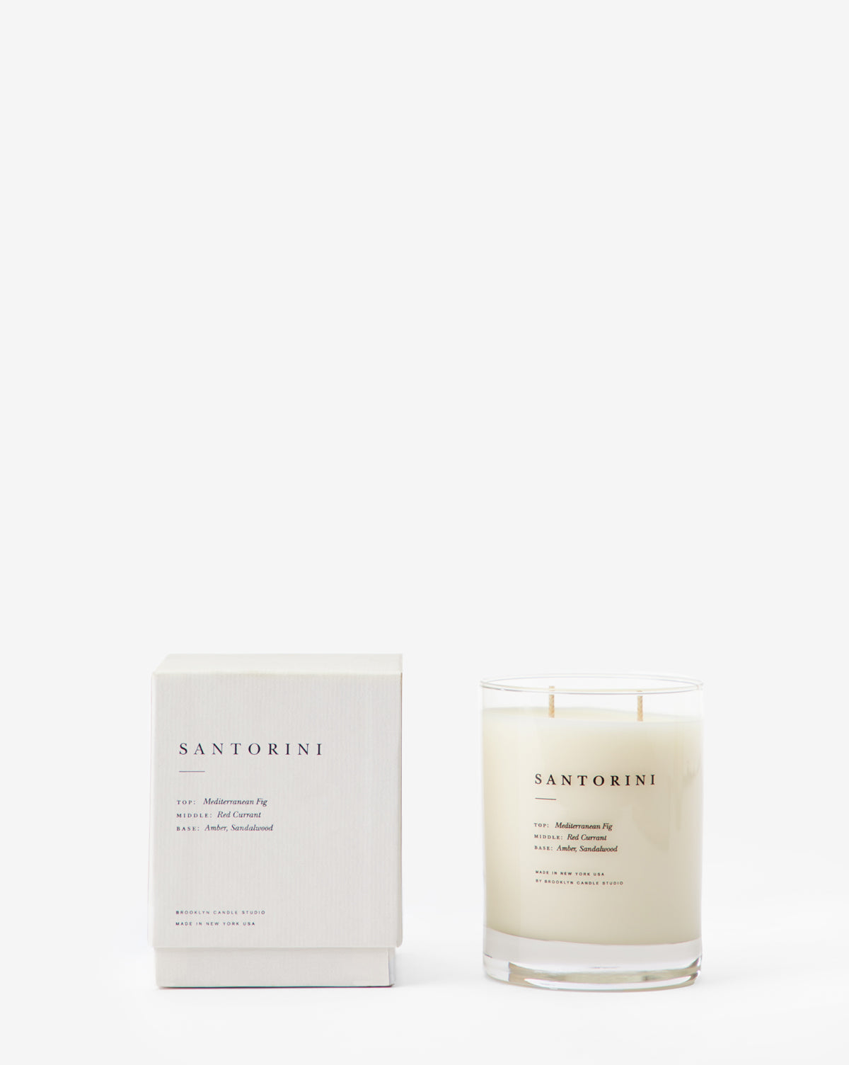 The Santorini Candle, crafted from soy wax, comes in a white glass jar with minimalist black text and a matching box. Its Mediterranean fig scent is highlighted against a clean white background.