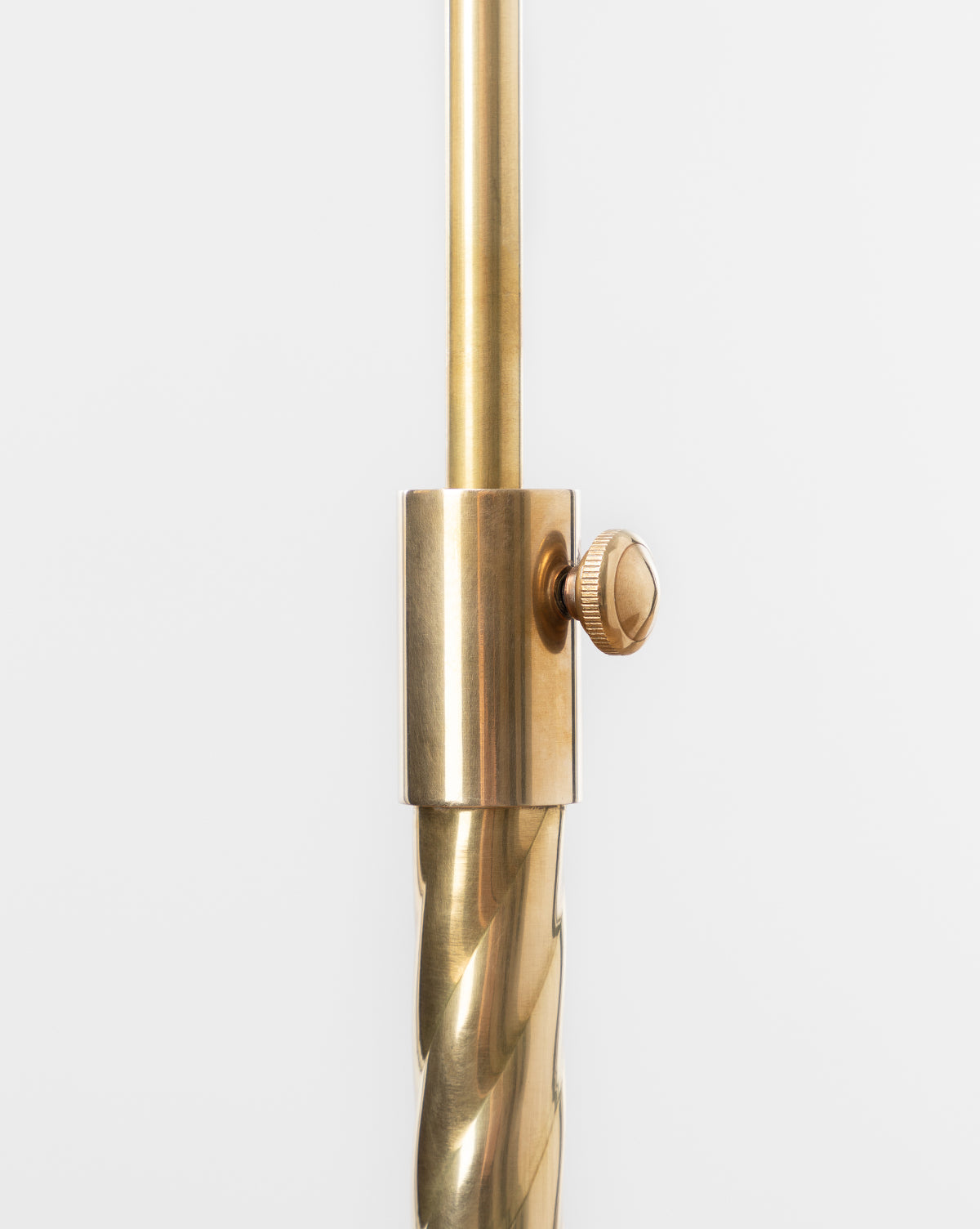 Close-up of the Saylor Floor Lamp’s brass adjustable rod with a knurled tightening knob and twisted lower section—an elegant detail—set against a plain white background, by McGee & Co.