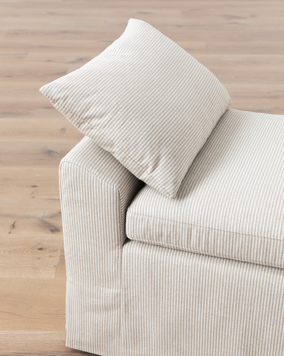 The Scaletta Bench (Ready to Ship) features beige and white ticking stripes, linen upholstery, a matching pillow, clean modern lines, and upholstered sides—perfectly set on a light wooden floor, by McGee & Co.