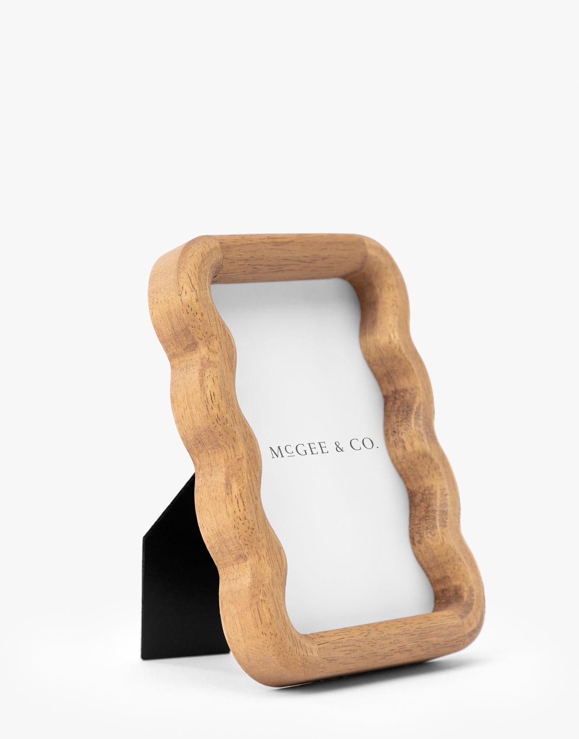 The Scalloped Wood Frame, made from natural rubberwood with a wavy edge and support stand, adds timeless elegance to any space. It displays a paper reading MCGEE & CO. on a white background by McGee & Co.
