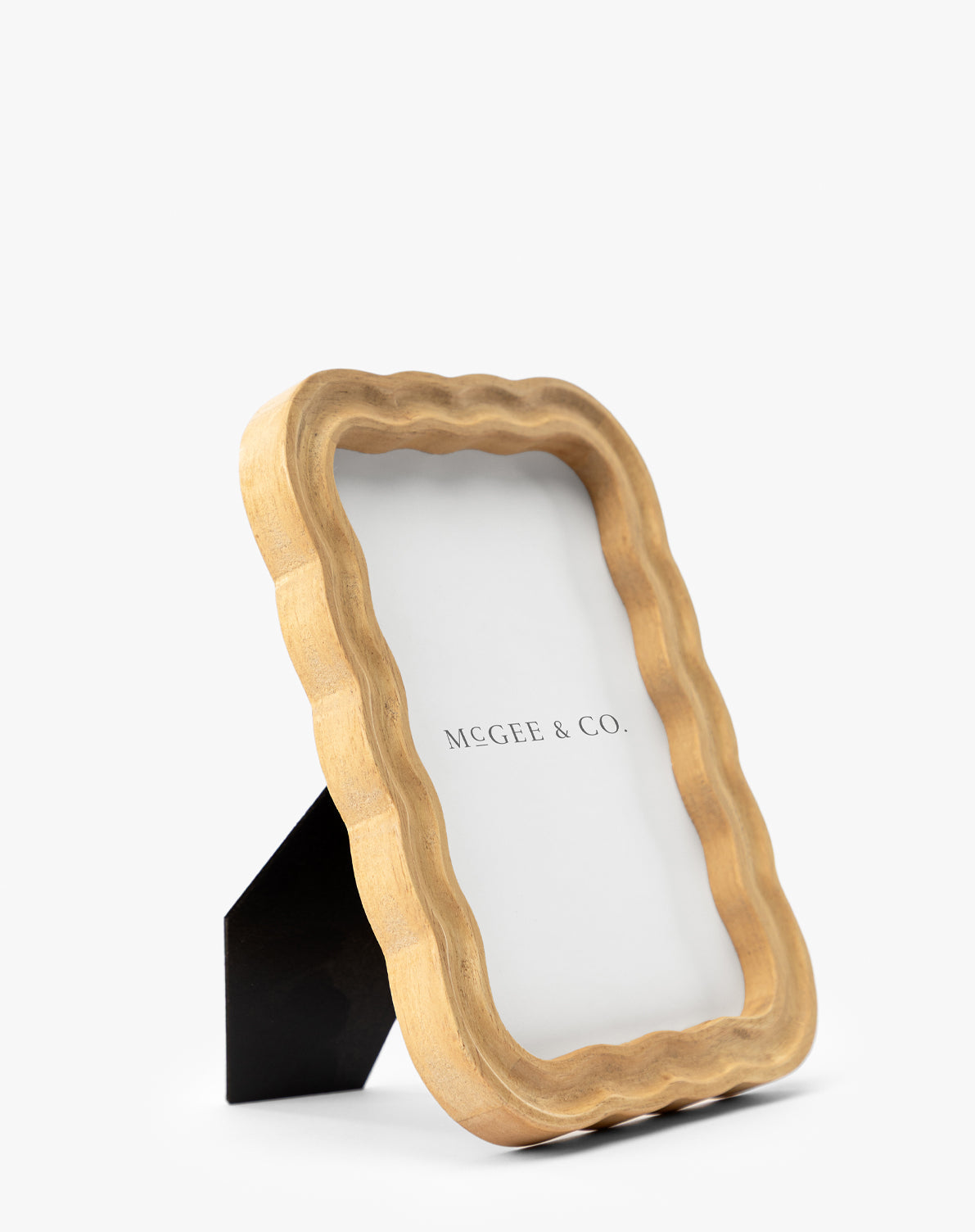 The Scalloped Wood Frame, made from natural rubberwood with a natural finish, stands upright on a black easel back and features a MCGEE & CO. placeholder against a white background—an elegant decor accent, by McGee & Co.