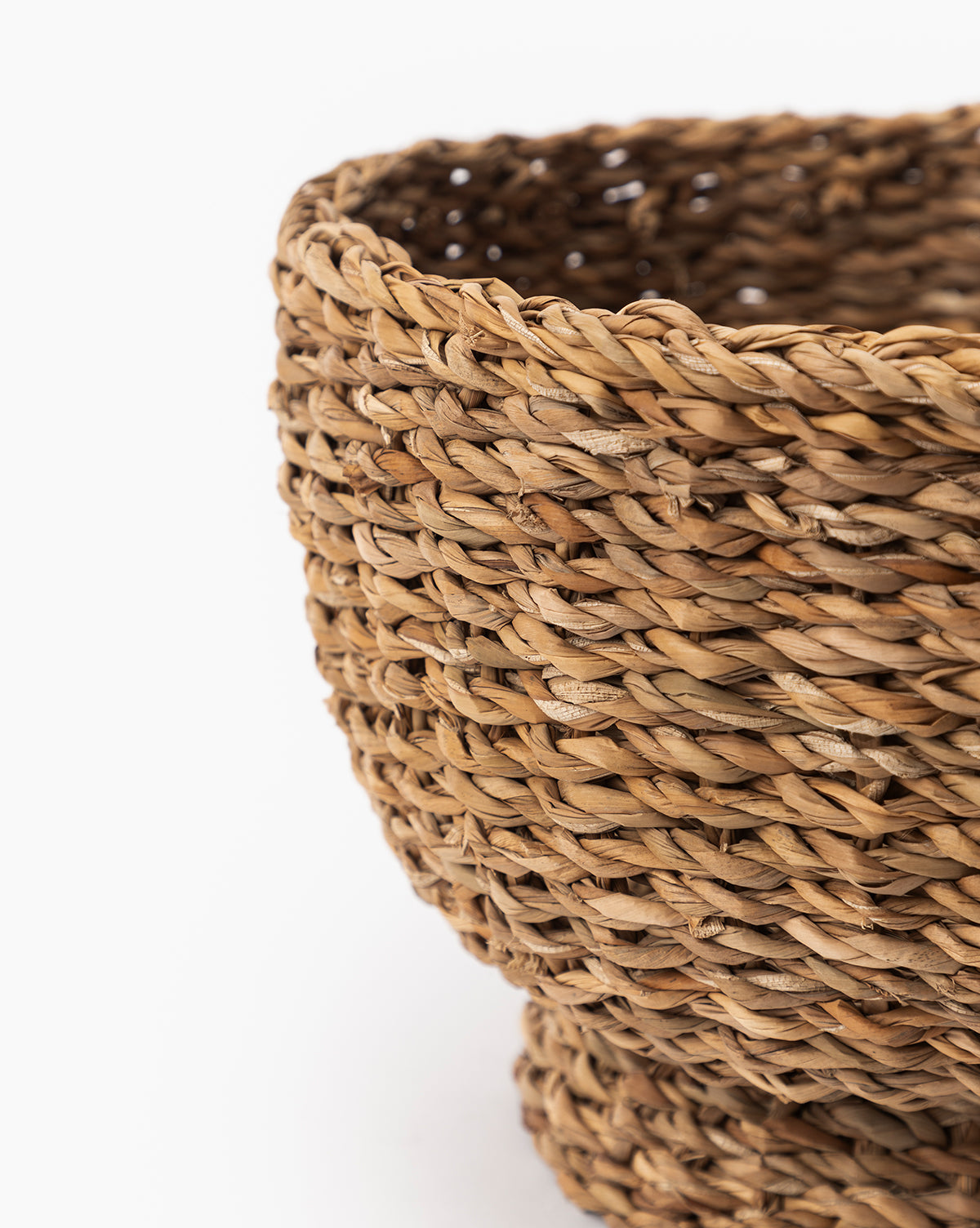 Close-up of the Seagrass Footed Bowl, crafted from natural brown fibers. The image highlights its textured, braided pattern and organic details, with only a portion of this decorative bowl shown against a white background.