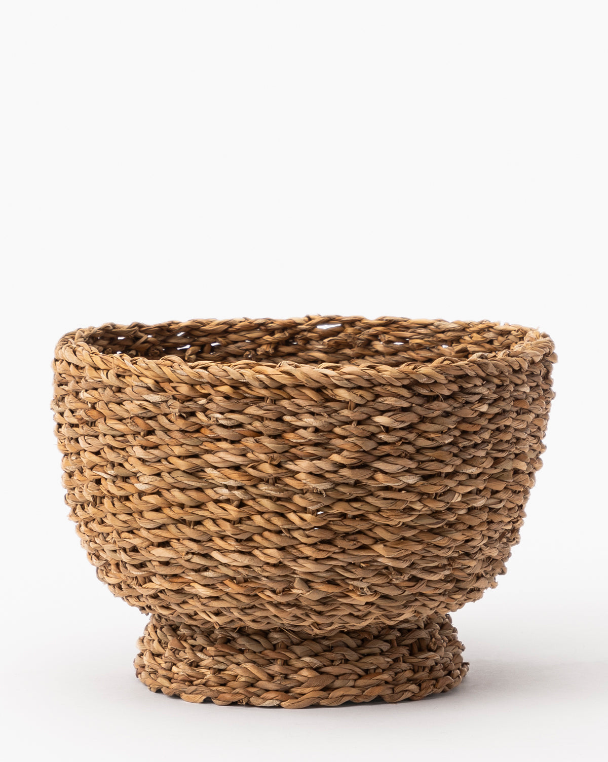 The Seagrass Footed Bowl showcases its natural brown fibers, wide opening, and sturdy raised base, highlighting beautiful details against a plain white background.