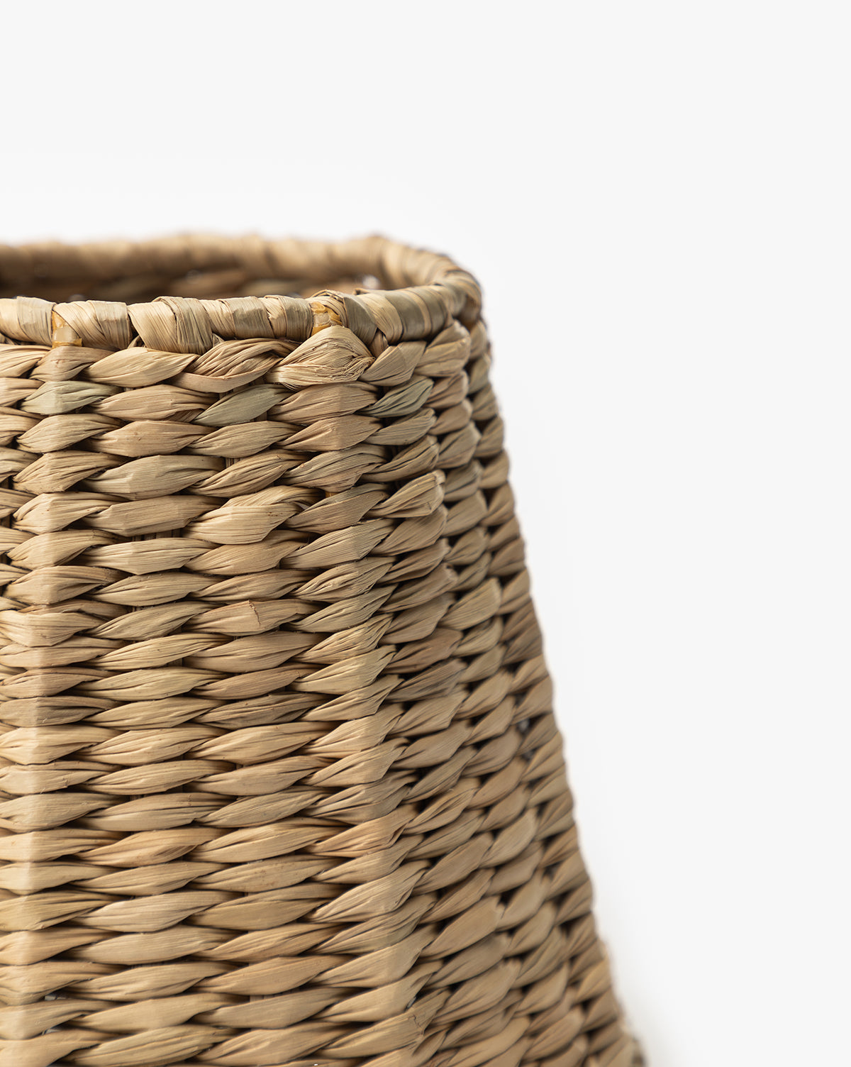Close-up of a woven, light brown Seagrass Lamp Shade against a white background showcases its detailed texture and craftsmanship. Only part of the shade’s top and side is visible, highlighting its stylish design, by McGee & Co.