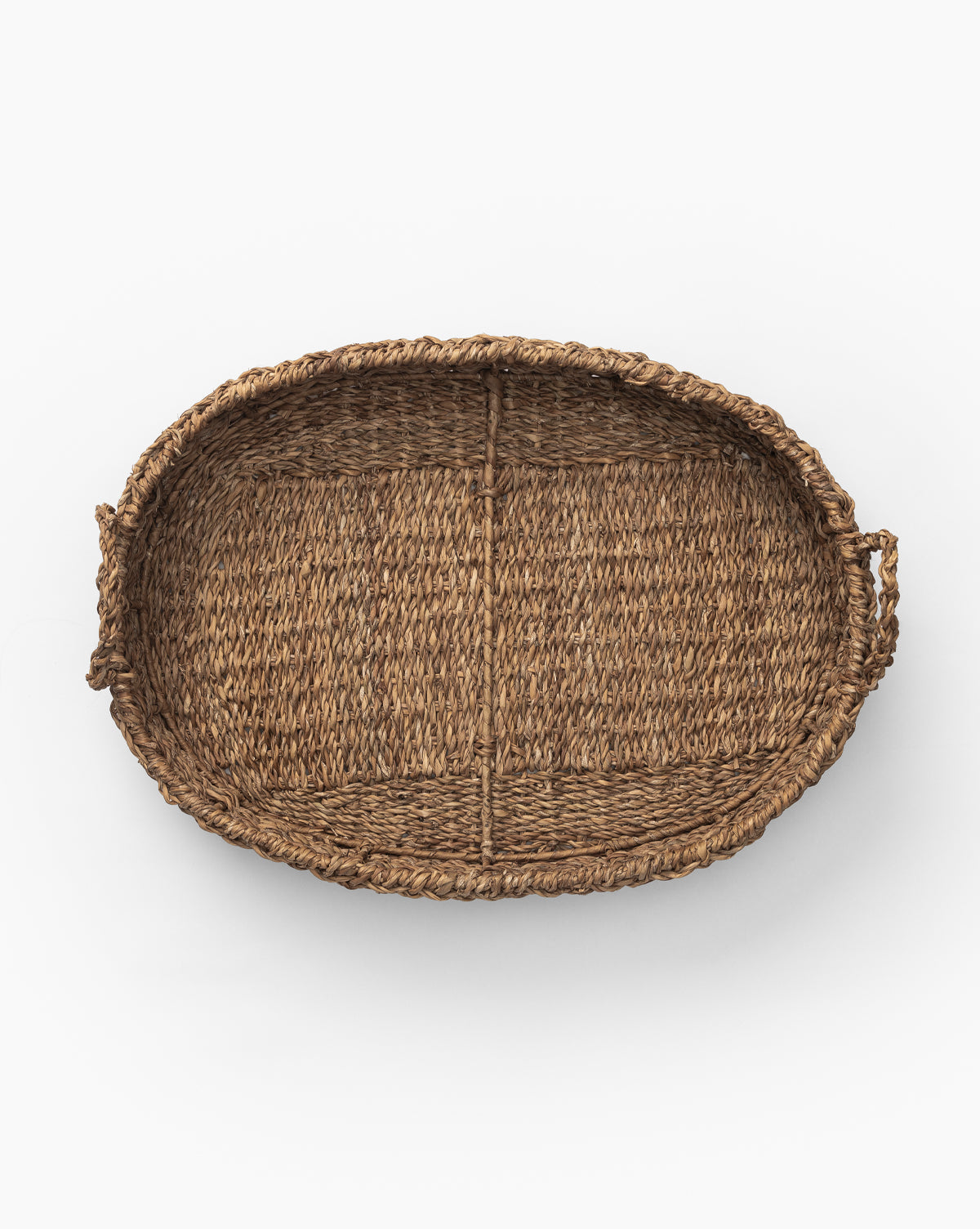 The Seagrass Oval Tray, crafted from natural brown wicker with raised edges and side handles, displays its decorative texture in an overhead view on a white background.