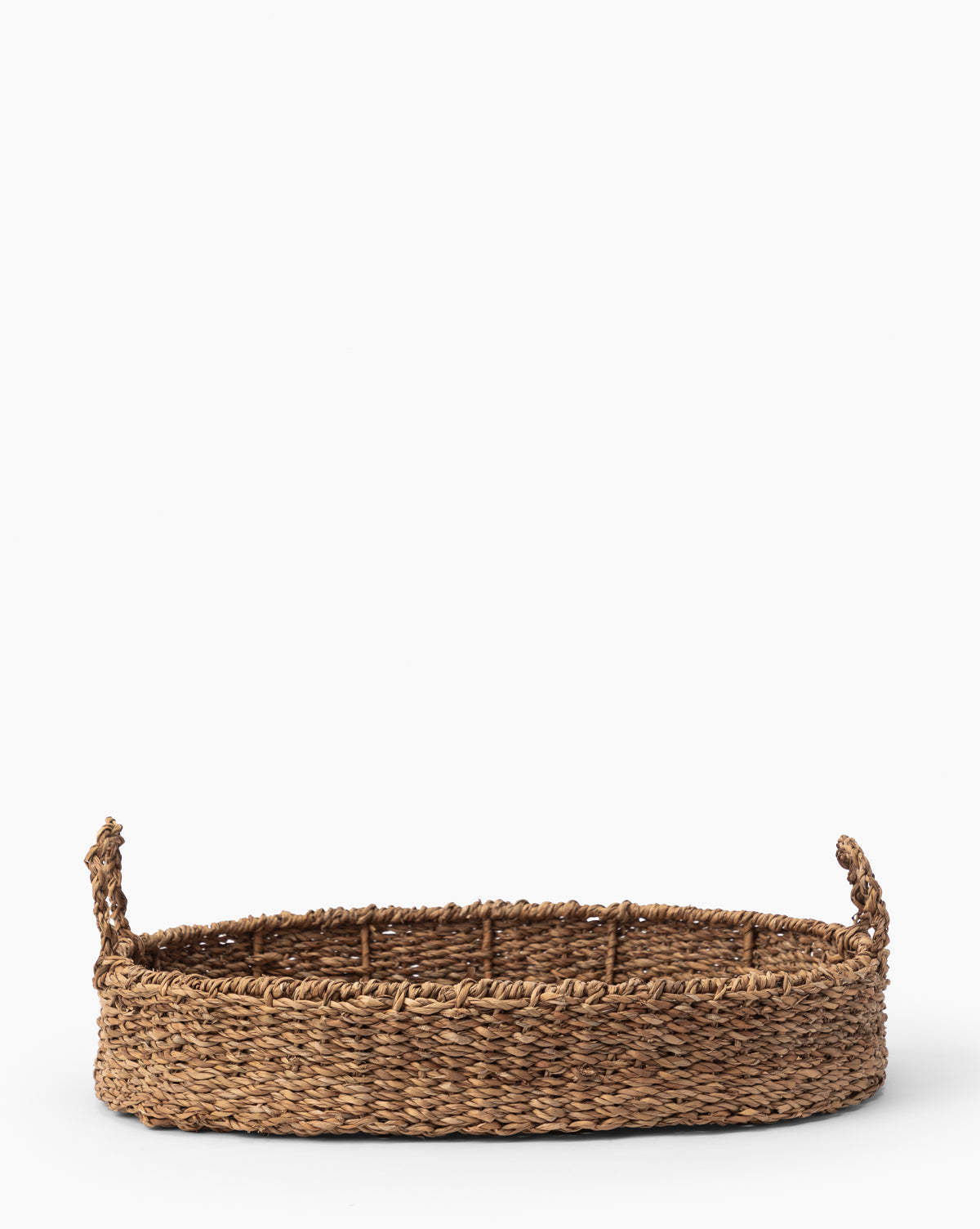 The Seagrass Oval Tray, featuring two handles and crafted from natural brown fibers, displays intricate natural details. Shown against a plain white background, this decorative tray adds rustic charm to any space.