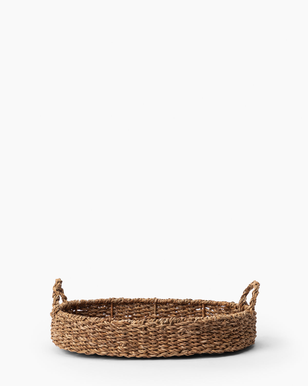The Seagrass Oval Tray, crafted from natural fibers with two looped handles and intricate woven details, is displayed against a plain white background.