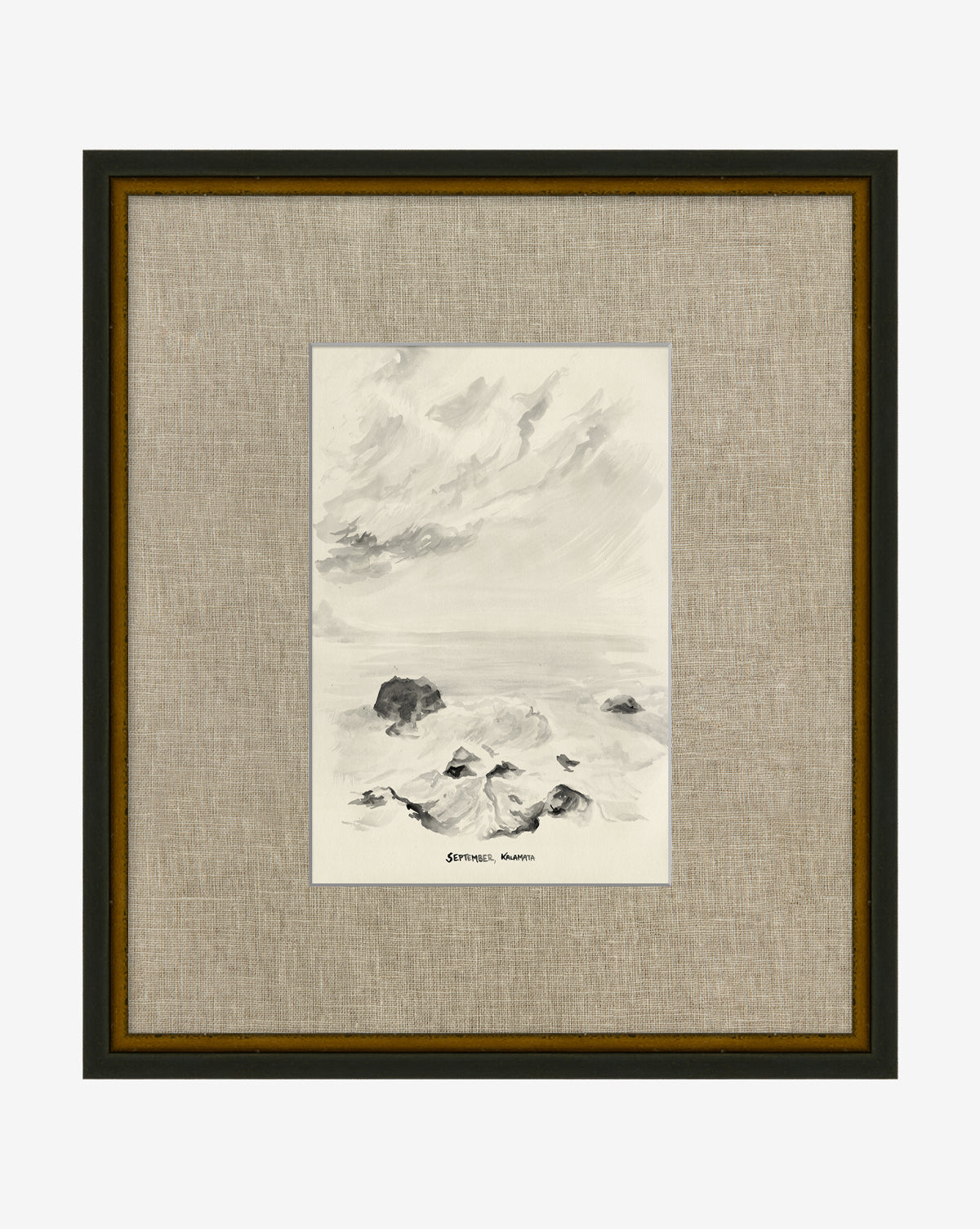 Framed black and white ink or watercolor painting titled September in Kalamata depicting a rocky shoreline under a cloudy sky. Features a hand-wrapped linen mat and a distressed black frame for an elegant finish.