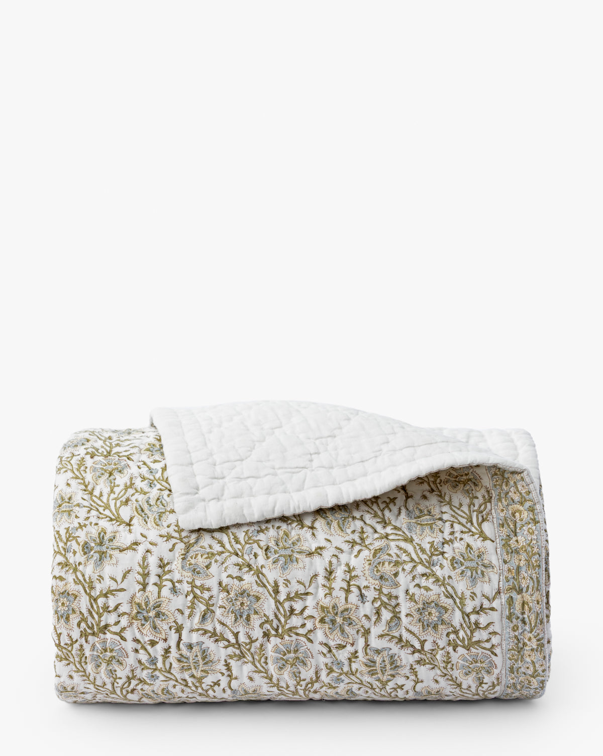 The Seton Kids Quilt by Renuka Inc. features a folded white design with green and beige floral patterns and textured stitching. One corner is turned over, revealing the plain white underside. McGee & Co.