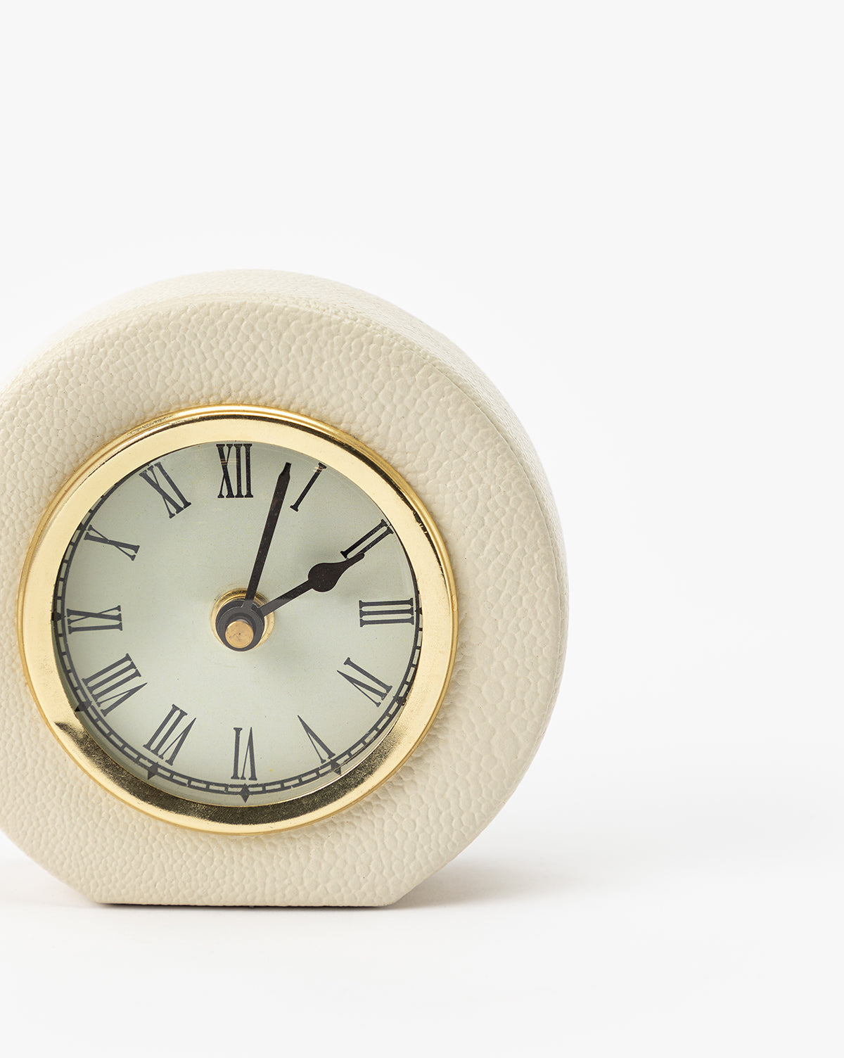 The Shagreen Table Clock is a small, round, elegant table clock with a gold rim, Roman numerals, and cream shagreen leather. It displays 8:05 against a plain white background.