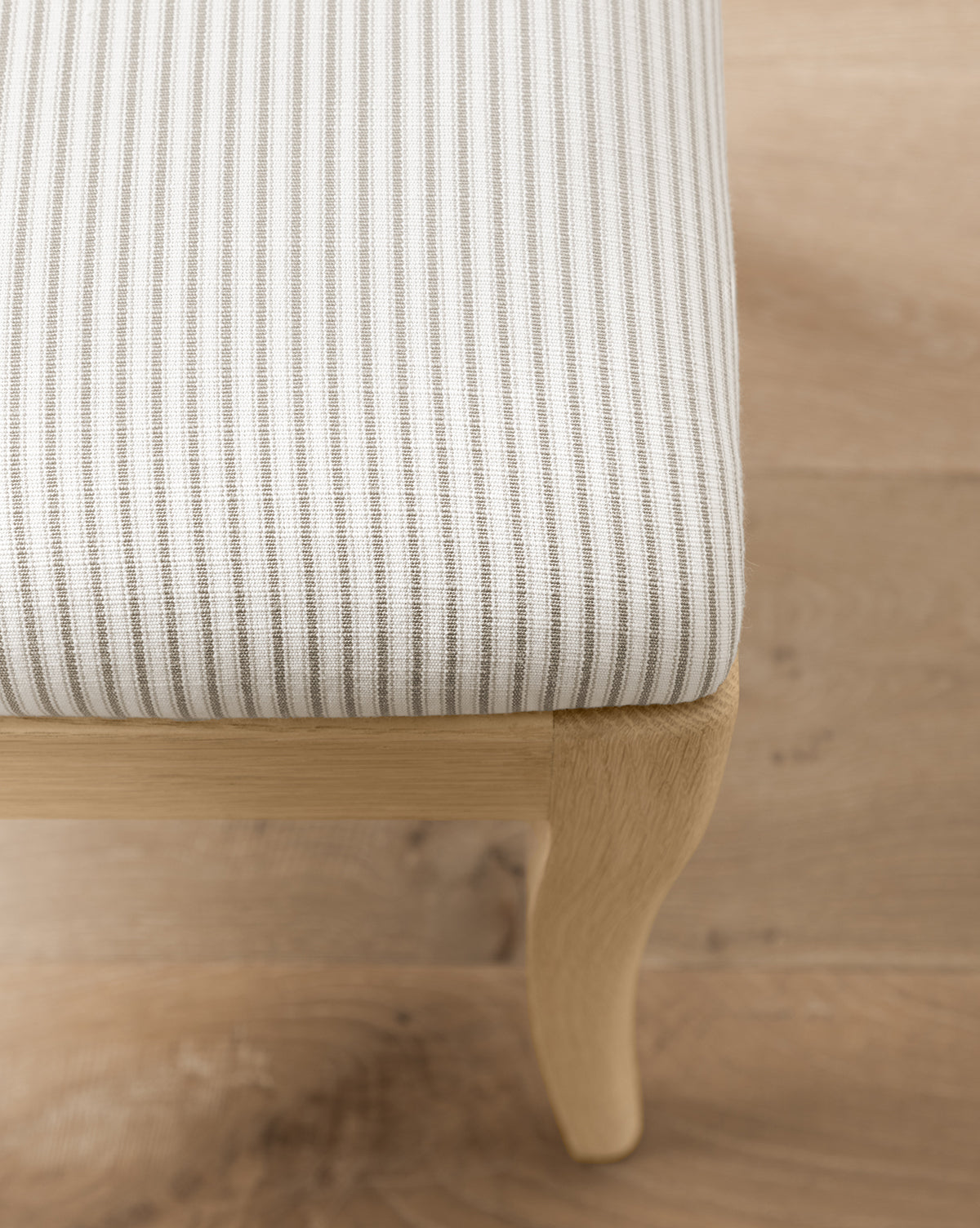 Close-up of the Makerspalm Shepherd Counter Stool, featuring light wood legs and a white seat with thin gray vertical stripes in performance upholstery, set on a light wood floor. McGee & Co.