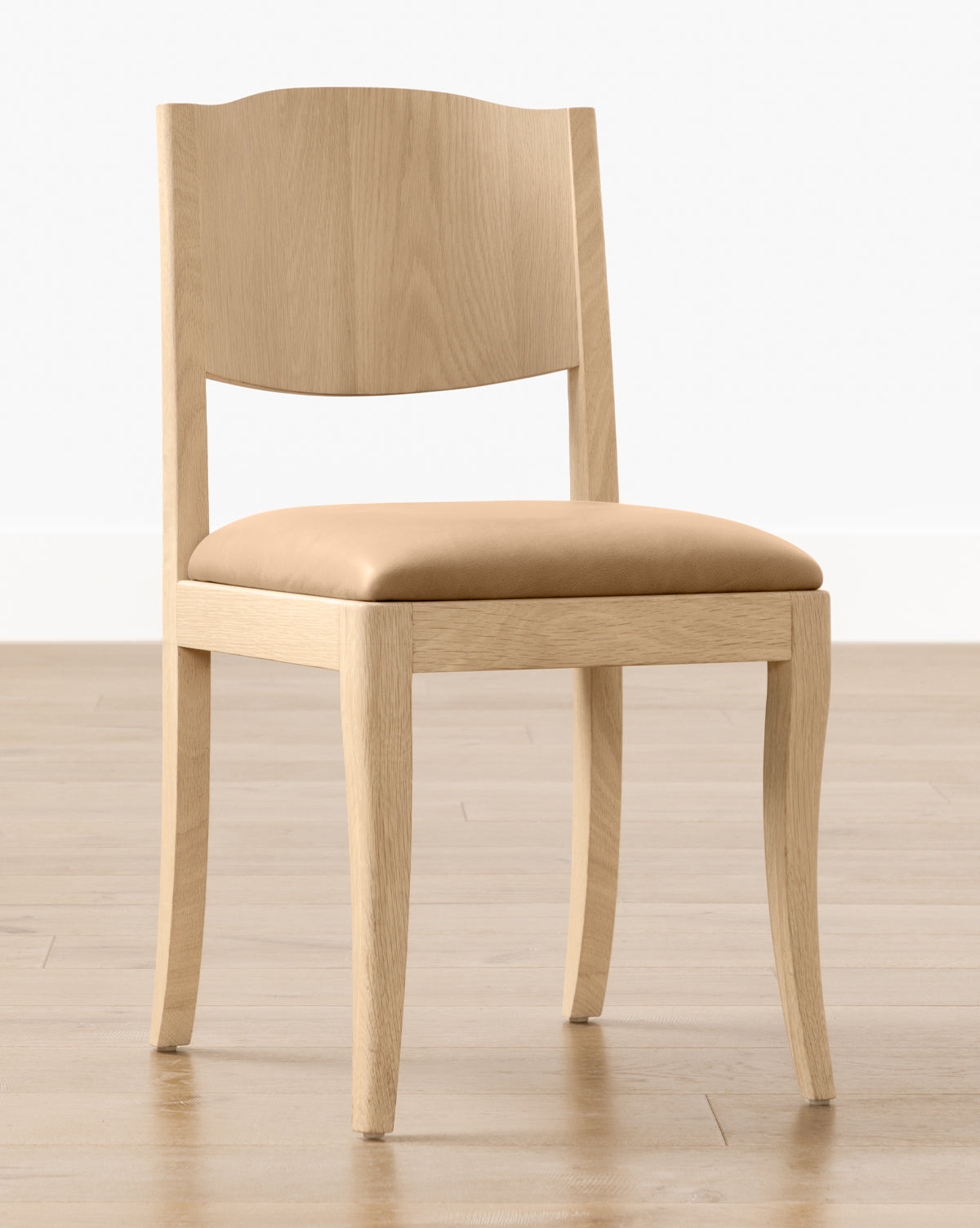 The Shepherd Dining Chair, featuring a white oak frame and a tan upholstered seat cushion, is placed on a light wood floor with a plain white wall in the background, by McGee & Co.