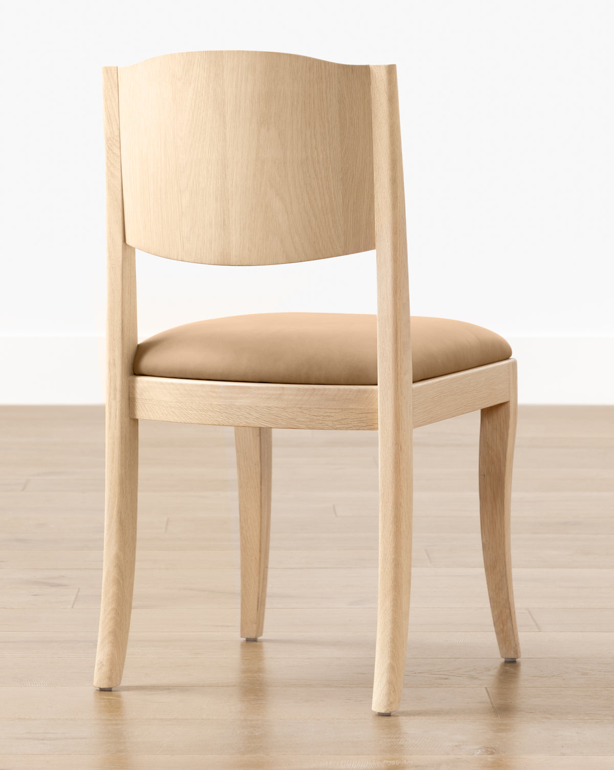 The Shepherd Dining Chair, featuring a white oak frame and tan upholstered seat cushion, is placed on a wooden floor against a plain white wall by McGee & Co.