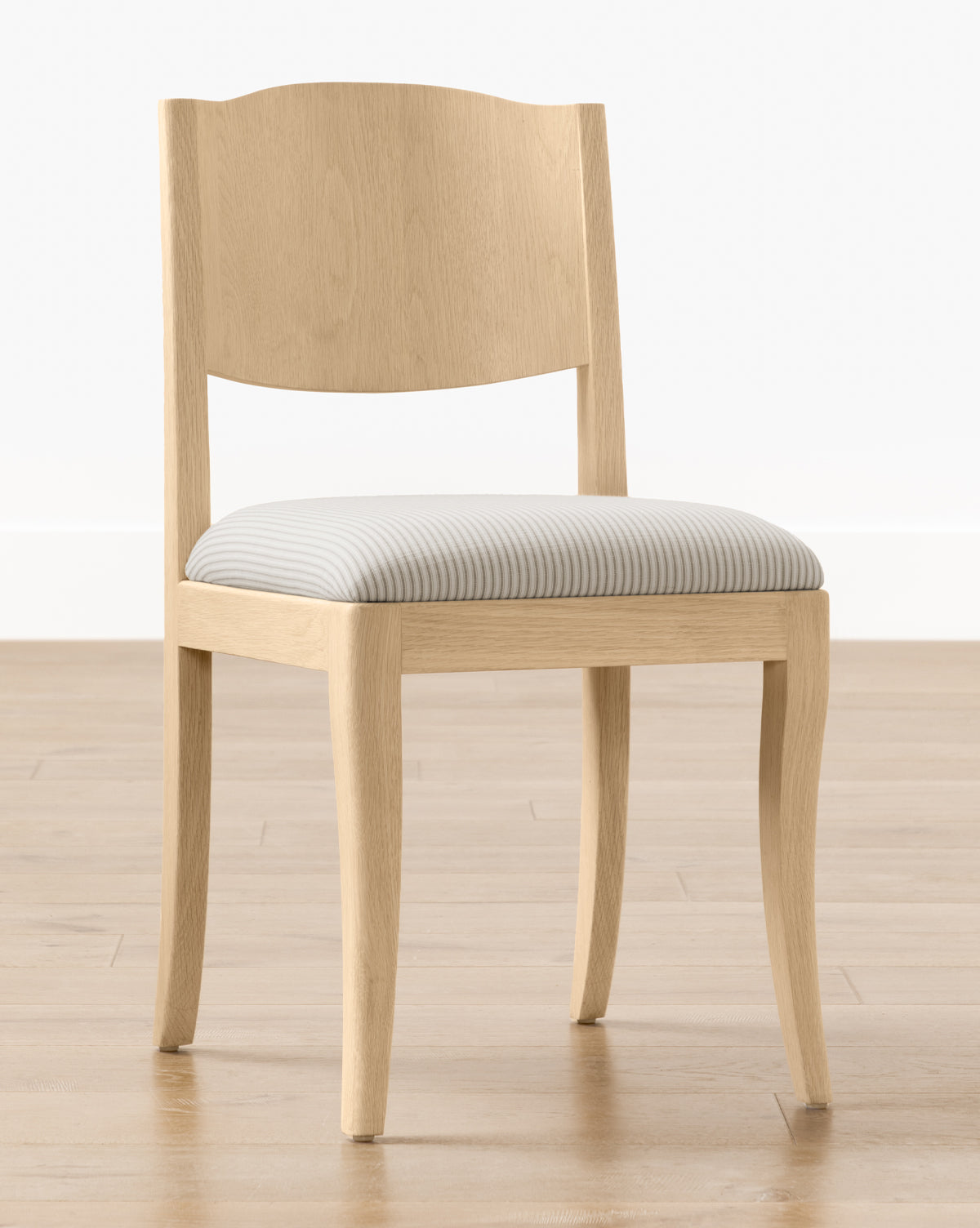 The Shepherd Dining Chair is a light wooden chair with a white oak frame, curved backrest, and a light gray and white striped upholstered seat cushion, shown on a wooden floor against a plain white wall by McGee & Co.