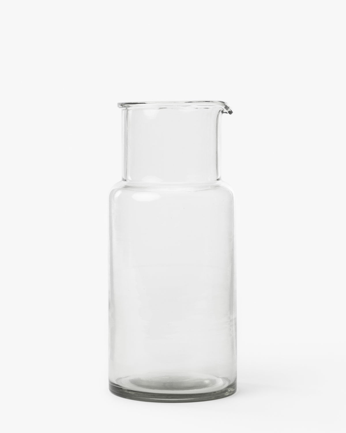The Sienna Carafe, made of clear hand-blown glass with a narrow spout, is shown upright on a white background—ideal for adding elegance to any dining setting, by McGee & Co.