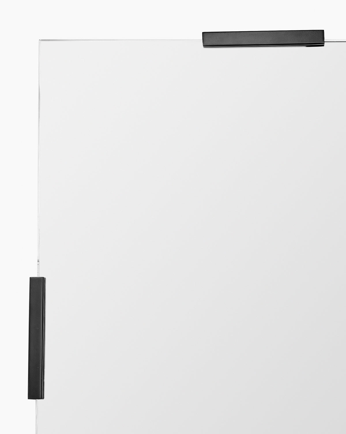 A close-up shows the top right corner of the Slade Mirror, a frameless design secured by two black metal brackets—one on the top and one on the right—against a white background, emphasizing its modern style, by McGee & Co.