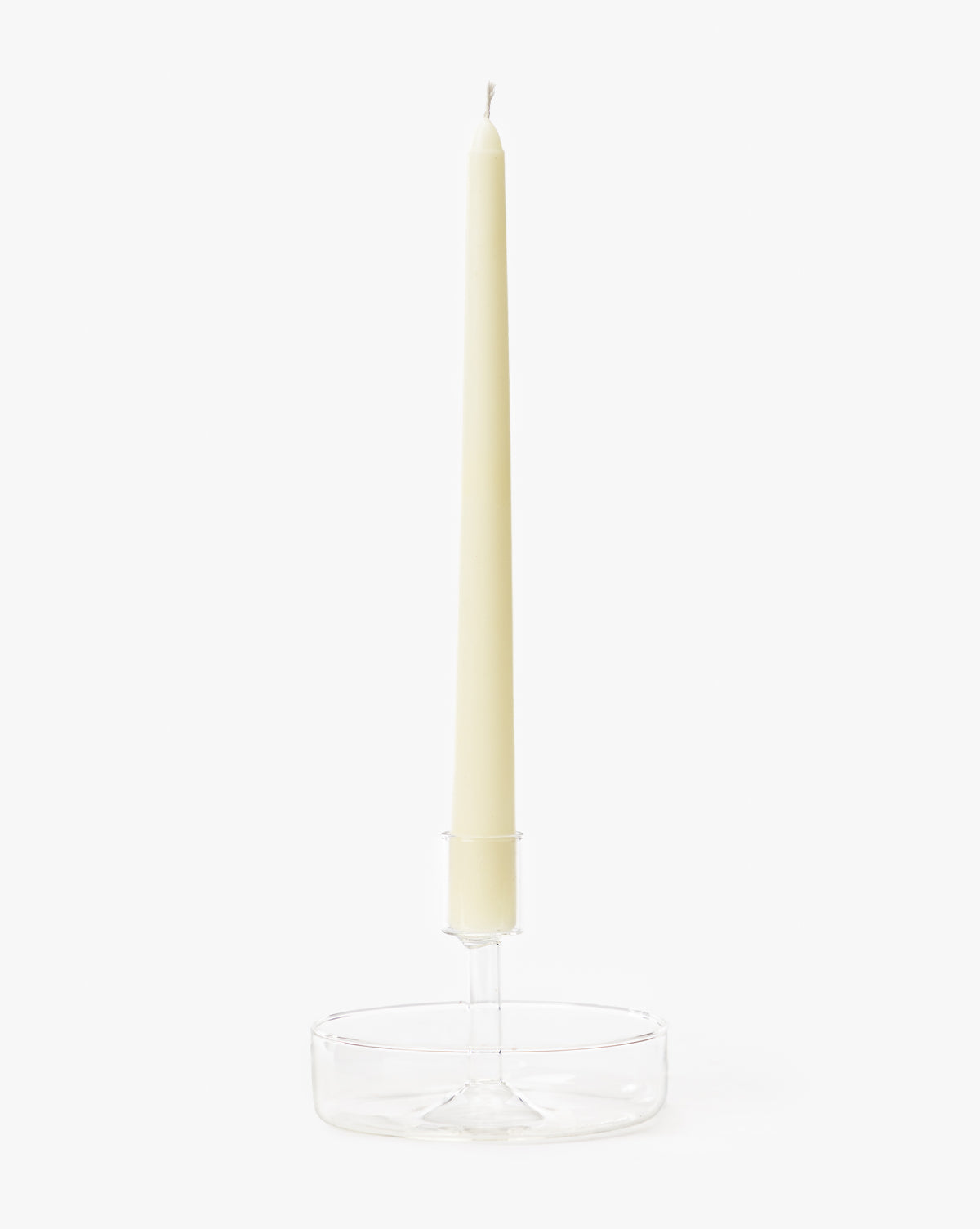 A tall cream candle stands upright in the Sofia Candle Holder, a clear glass taper holder, set against a plain white background.
