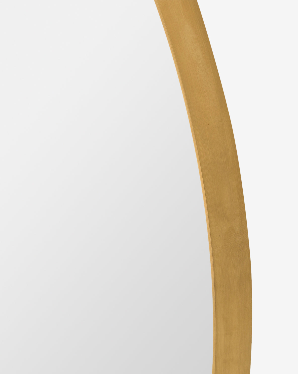 Close-up of the Solange Mirror, featuring a minimalist design with a gold-colored, rounded frame and partial brass finish against a white background. Only part of the mirror’s reflective surface and elegant edge are visible by McGee & Co.