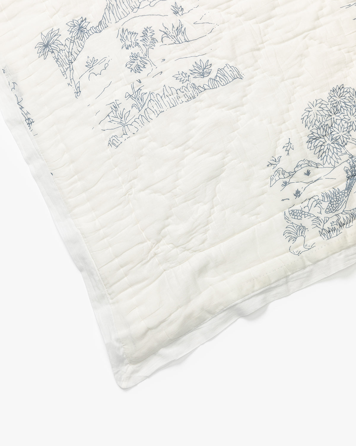 A corner of the Solano Block Print Kids Quilt by Indaba shows white cotton bedding with delicate blue line drawings inspired by nature scenes—trees, plants, and animals—creating a soft, charming look for kids. McGee & Co.