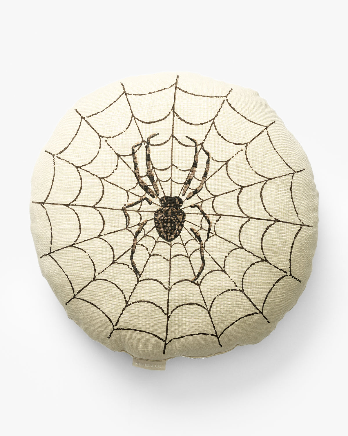 The Spider Pillow is a round beige cushion with a black spider and an embroidered web design covering the surface—an ideal Halloween decor accent, by McGee & Co.