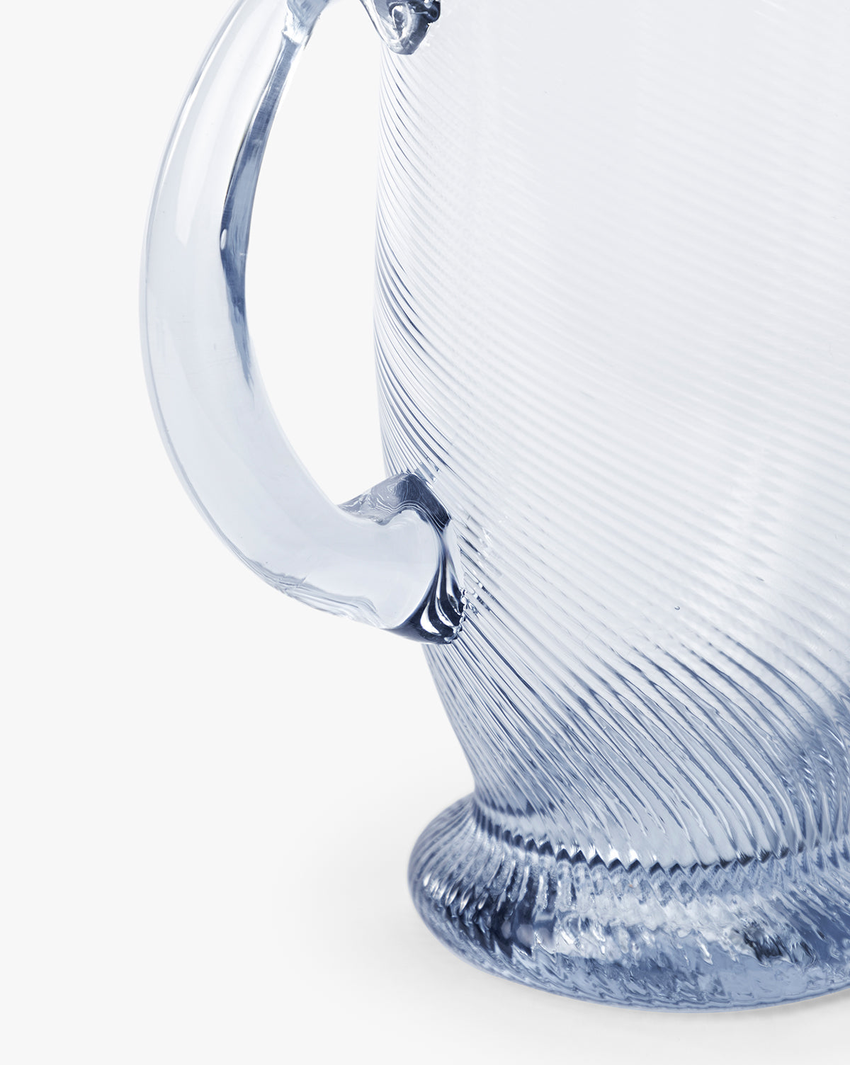 Close-up of the Spiral Jug, a handcrafted glass jug with a curved handle and ridged base, perfect for any tabletop setting, shown against a white background, by McGee & Co.