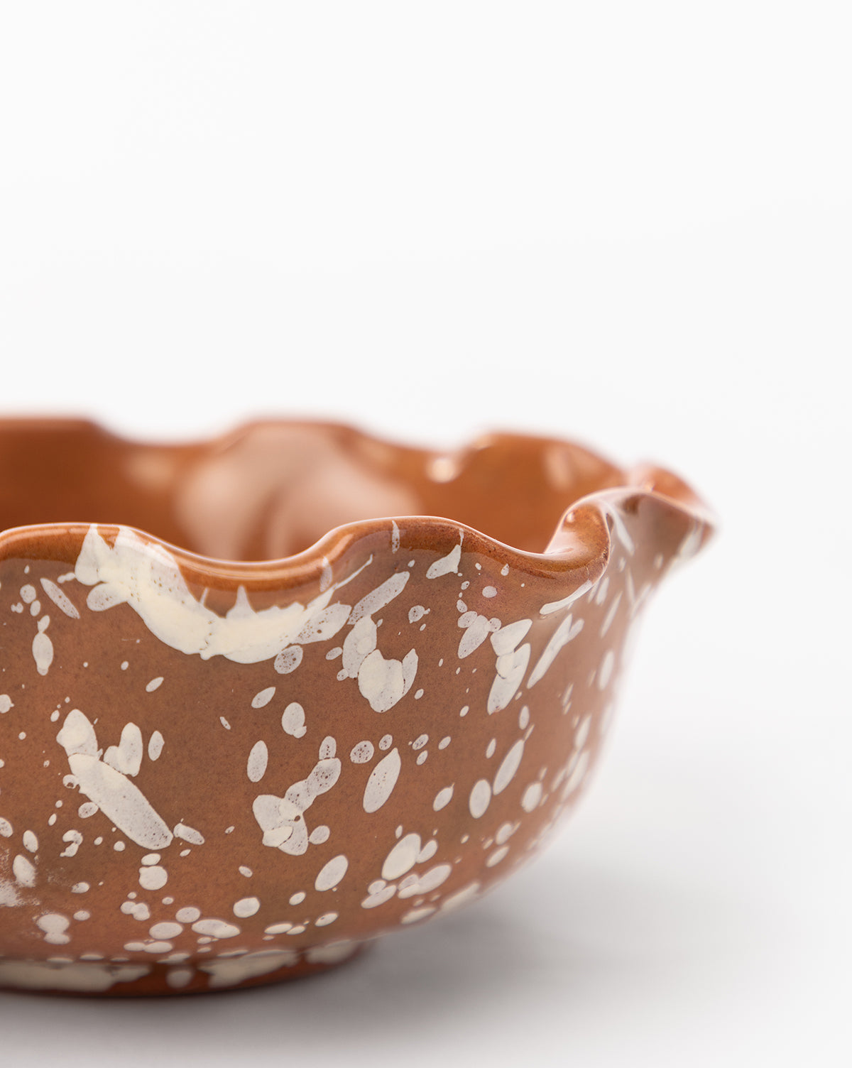 A close-up of the Splatter Scallop Dish, an artisan ceramic bowl with a wavy rim and white speckled patterns, set against a plain white background by McGee & Co.