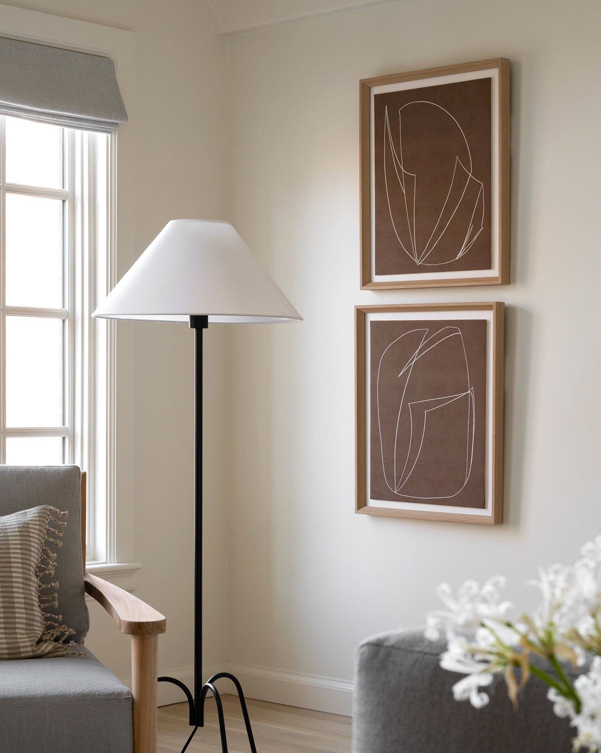 A cozy corner features a gray armchair, black floor lamp with white shade, and the Contour Study II framed giclée print on a cream wall by the window, with white flowers in the foreground.