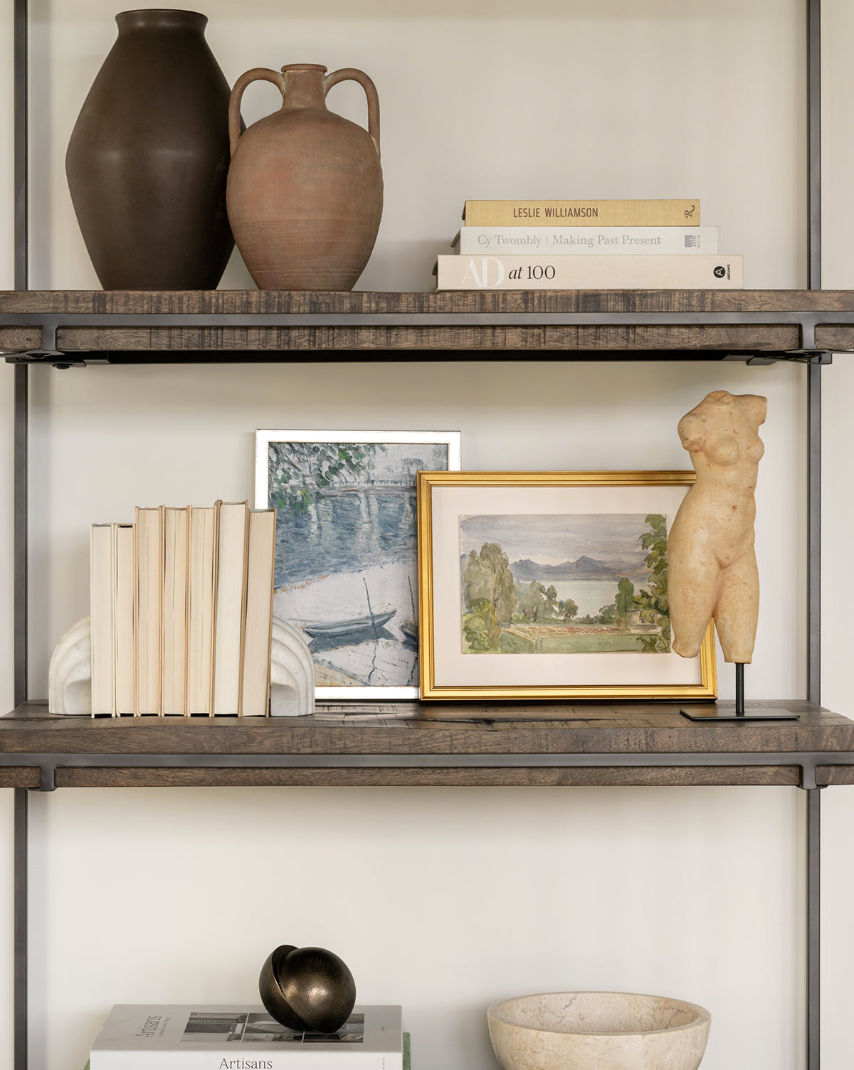 A neatly styled shelf features the Jackson Offset Sphere alongside ceramic vases, stacked books, framed art, a torso sculpture, and decorative objects—all arranged in a minimalist, neutral-toned setting.