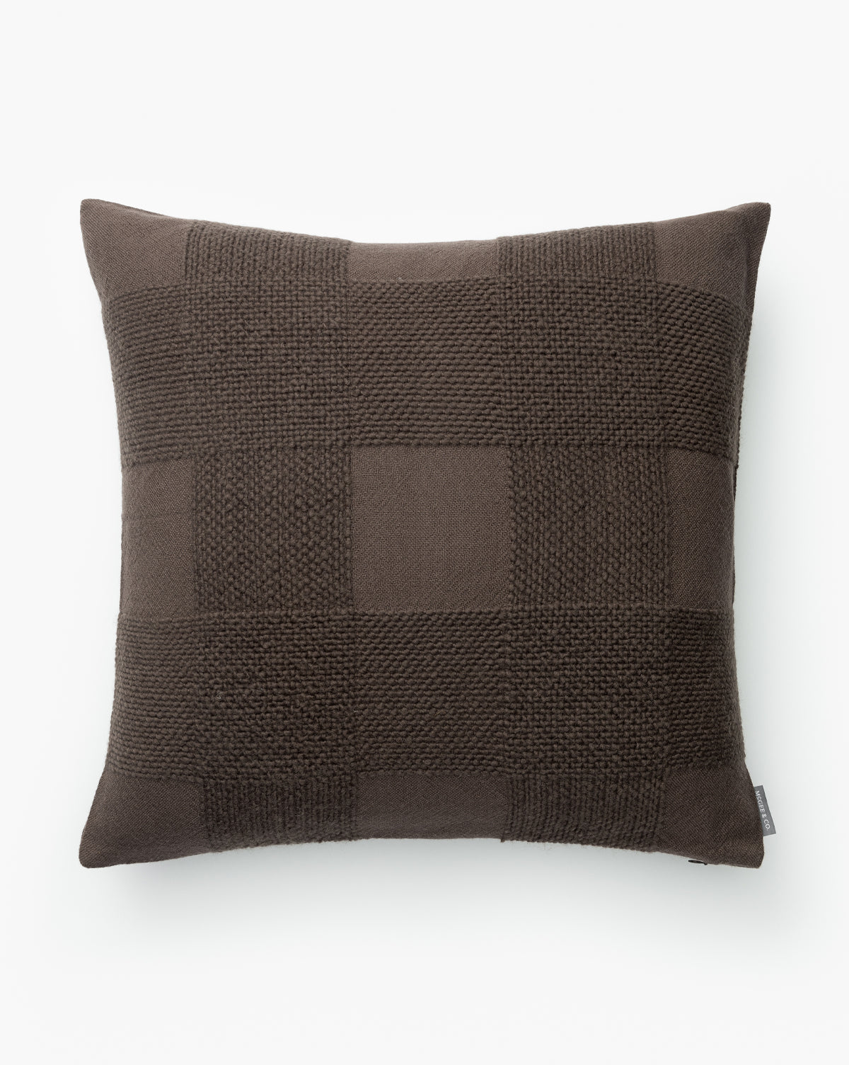 The Stanley Pillow Cover is a square, dark brown cover with a checkerboard pattern of smooth and textured knit squares, made from wool and featuring a woven design, shown on a white background by McGee & Co.