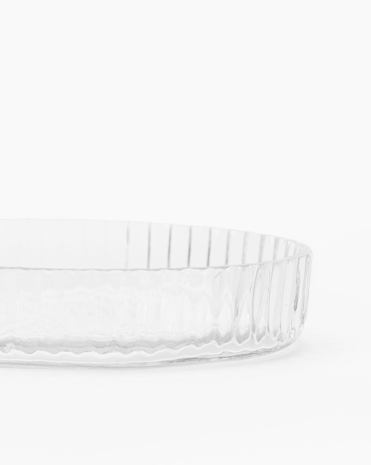 A clear, round dish from the Stein Glass Collection features vertical ridges and is shown against a white background. This elegant blown glass piece, partially visible in the photo, is ideal for displaying on a bathroom countertop.